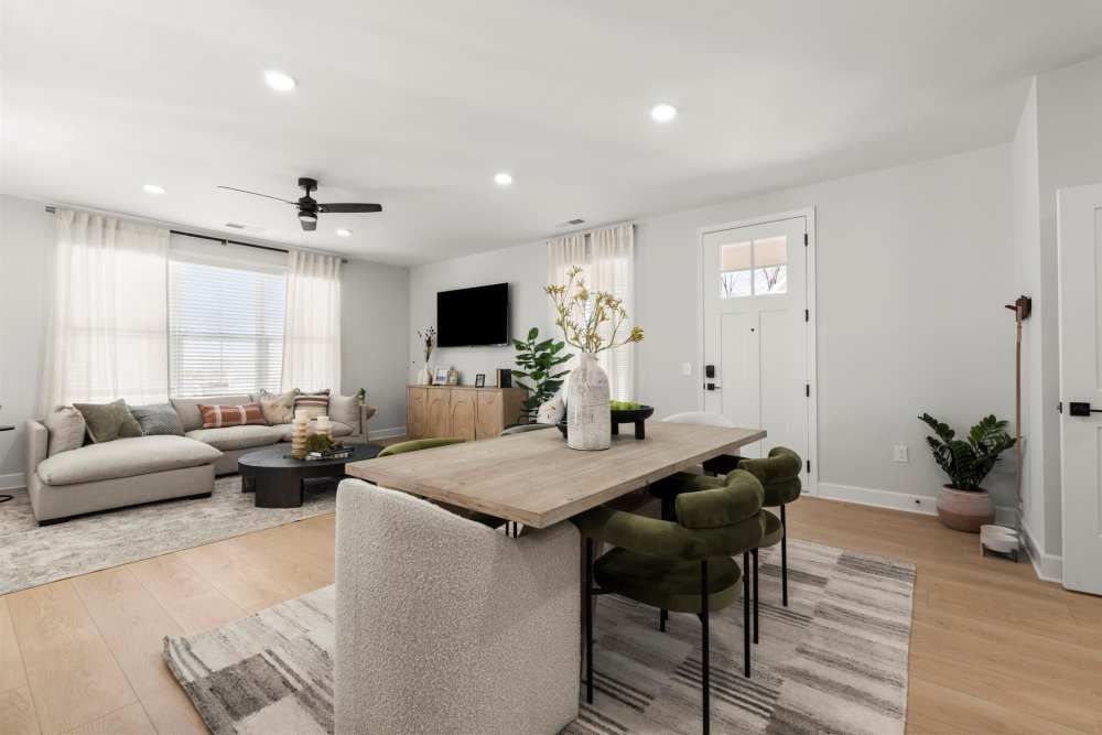 Open-plan living room with dining area at Hayloft Big Creek, offer 55+ homes for rent in Alpharetta, GA. Light-colored walls, wood floors, modern furniture, and a tv.