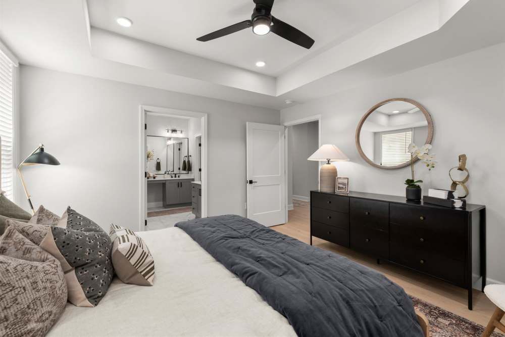 Bedroom with gray walls, white bed, dark dresser, round mirror.