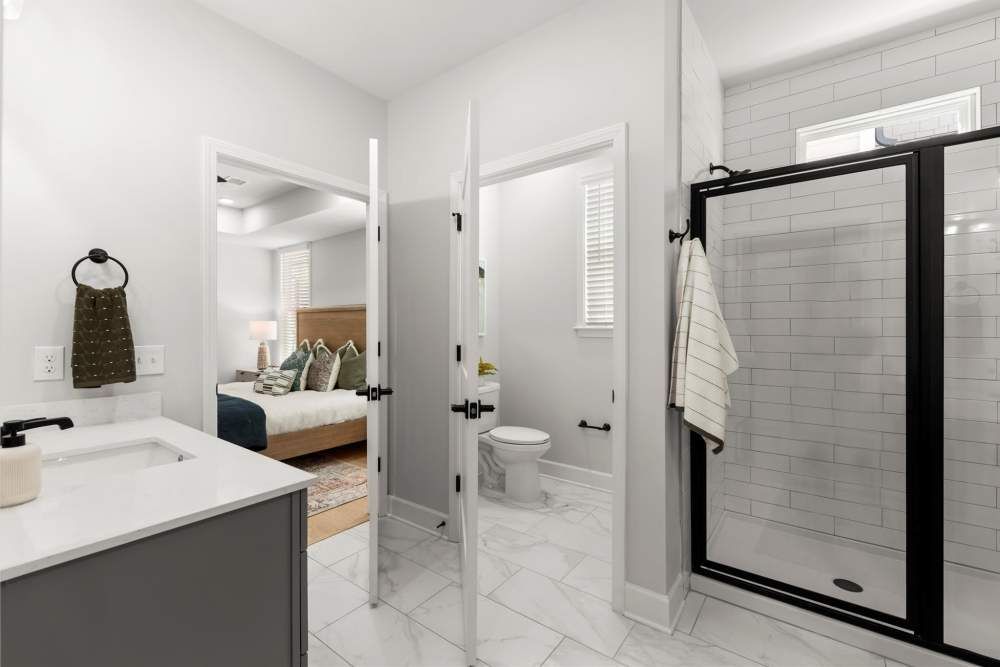 Bathroom with gray vanity, toilet, shower, and door to bedroom at Hayloft Big Creek, offer 55+ senior apartments for rent in Alpharetta, GA.