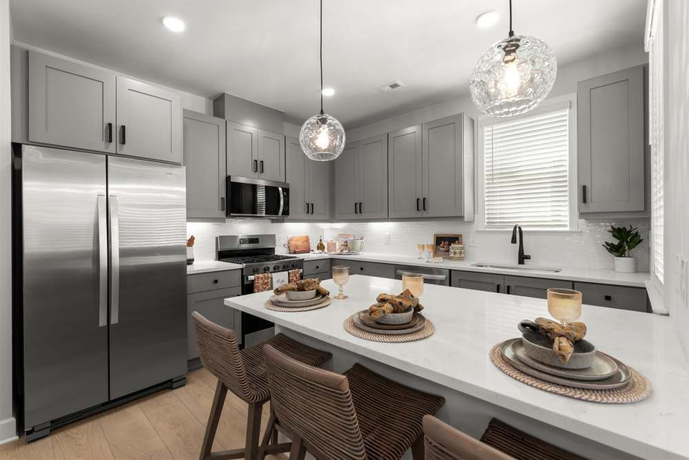 Modern gray kitchen with stainless steel appliances, white countertops, and island with stools at Hayloft Big Creek, offer newly built 55+ community for rent in Alpharetta, GA.