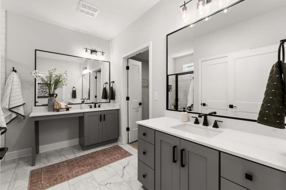 Modern bathroom with gray cabinets, white countertops, and black-framed mirrors at Hayloft Big Creek, offer 55+ apartments for rent in Alpharetta, GA.