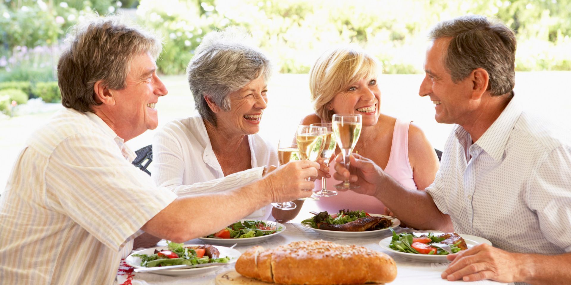Four people toasting with champagne at an outdoor meal, smiling and laughing.