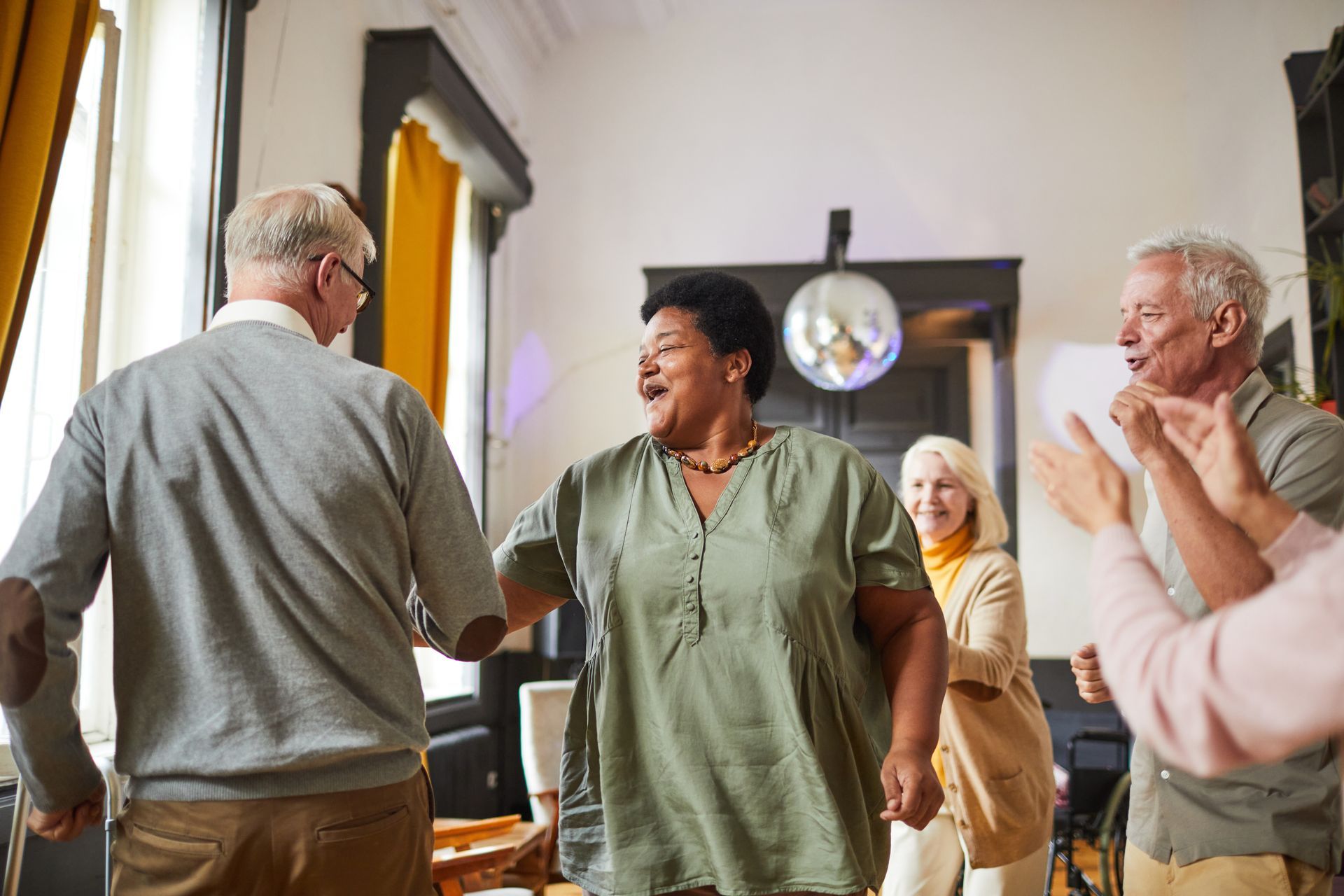 Group of older adults dancing happily indoors, smiling and clapping.