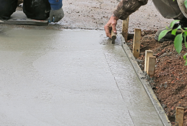 A man is spreading concrete on a sidewalk with a trowel.