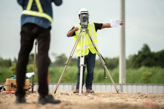 a man is standing next to a man using a theodolite on a tripod .