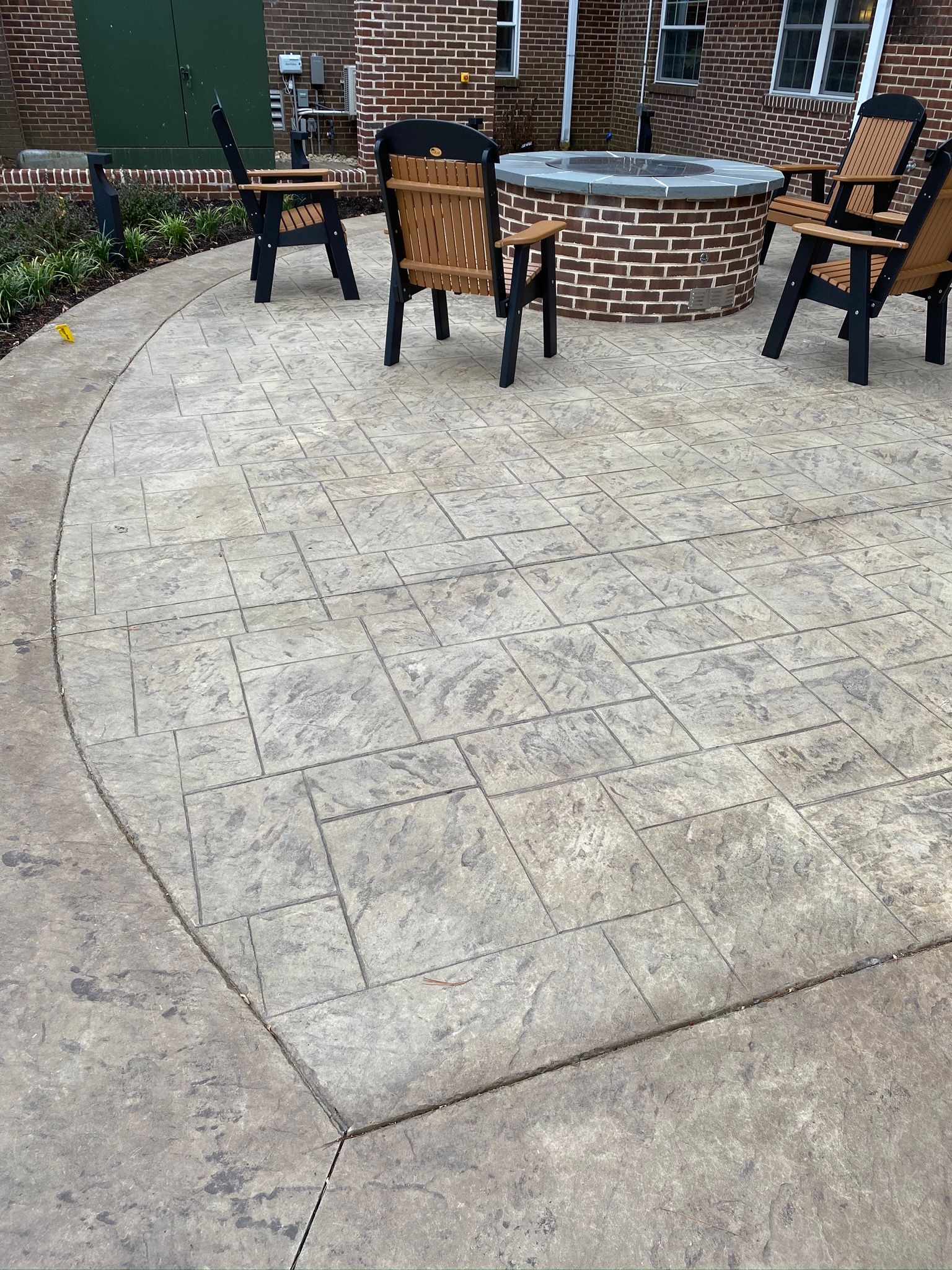 a stamped concrete patio with a fire pit and chairs in front of a brick building