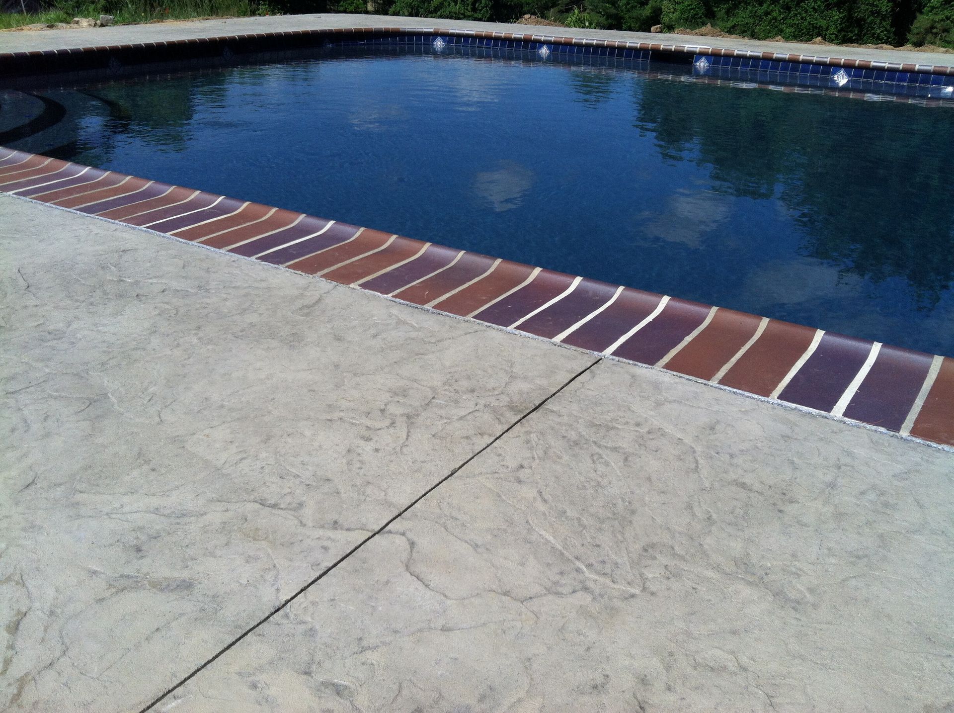 a  stamped concrete swimming pool deck with a brick look border and a textured concrete deck