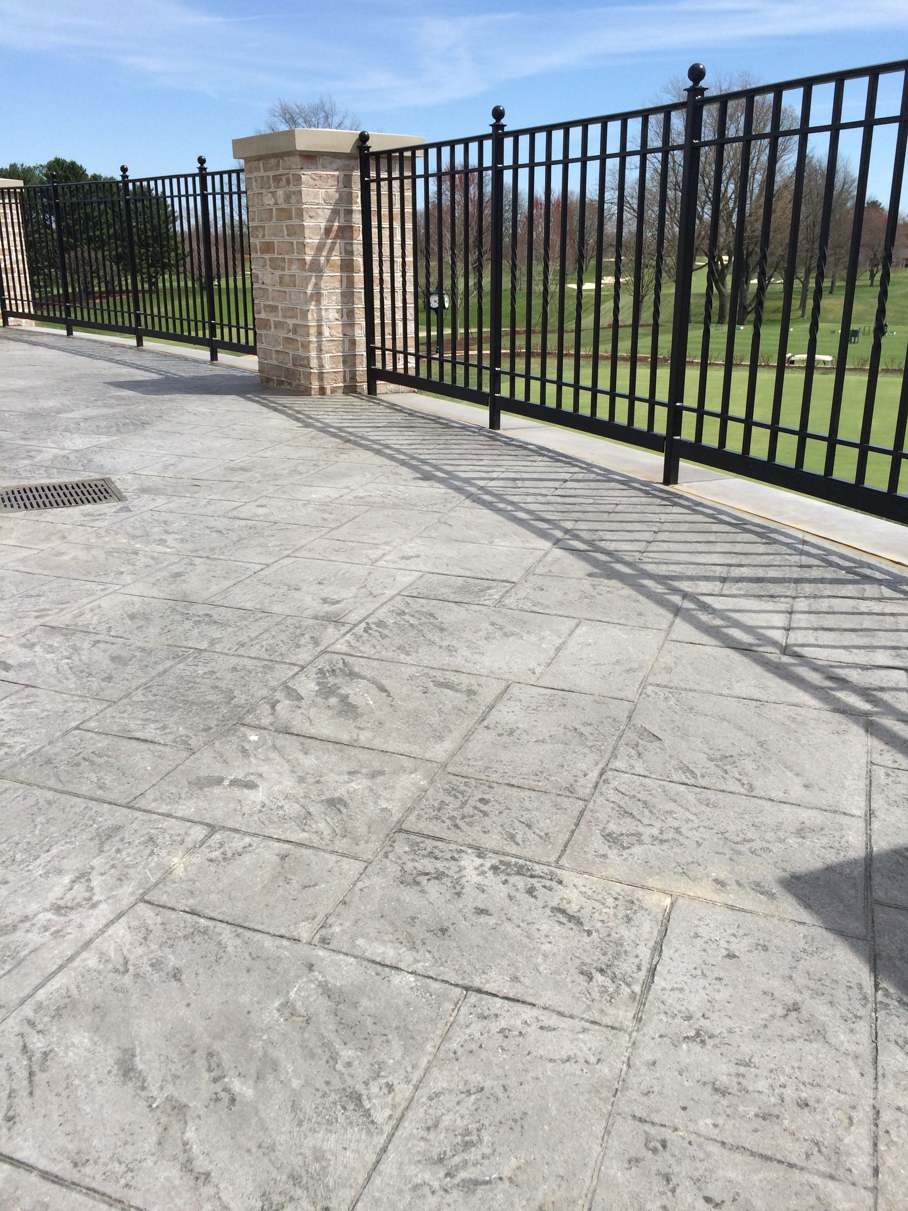 a fence surrounds a stamped concrete patio with a view of a golf course .