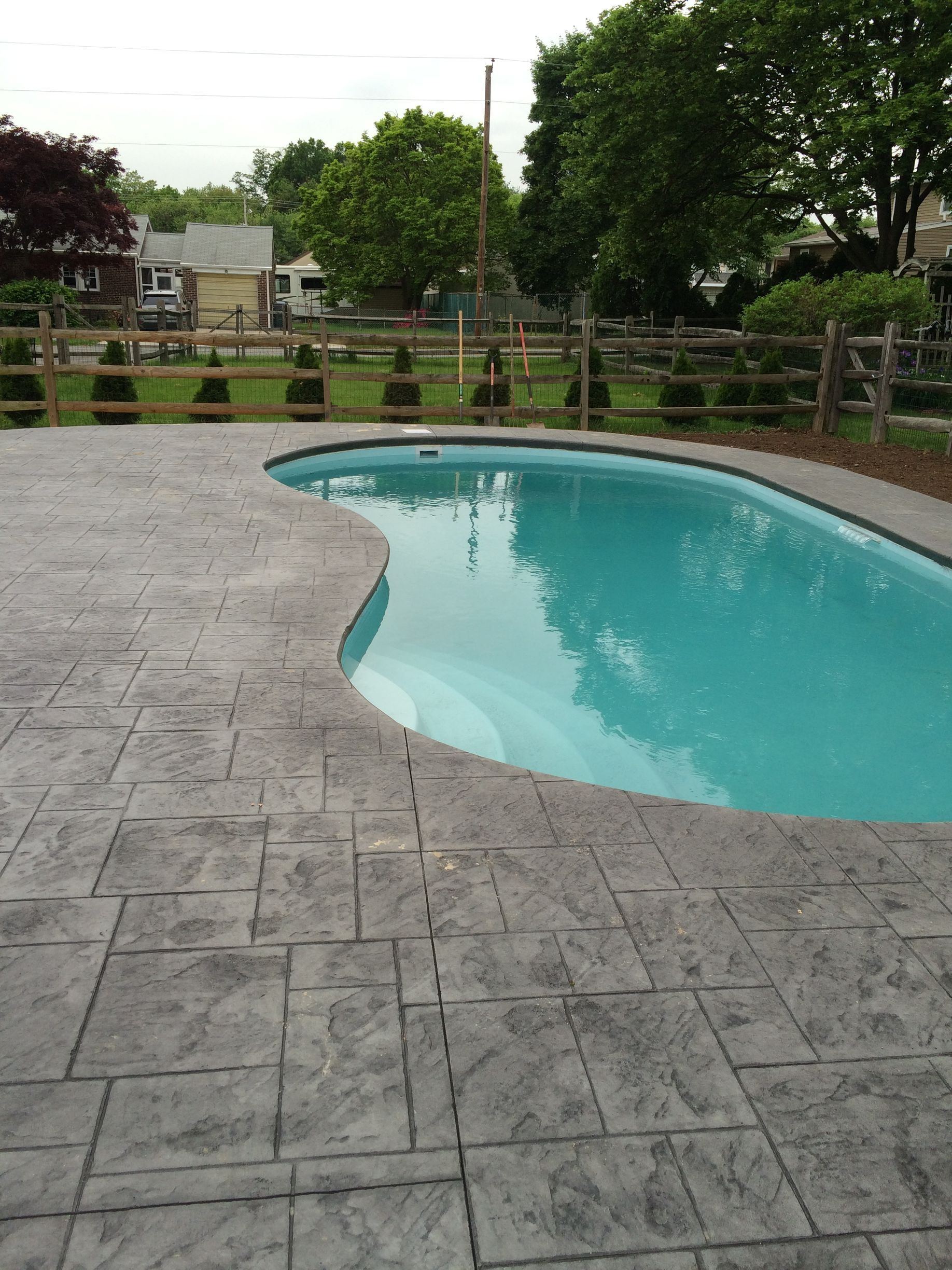 a large  stamped concrete 
 slate-like swimming pool deck with a fence in the background