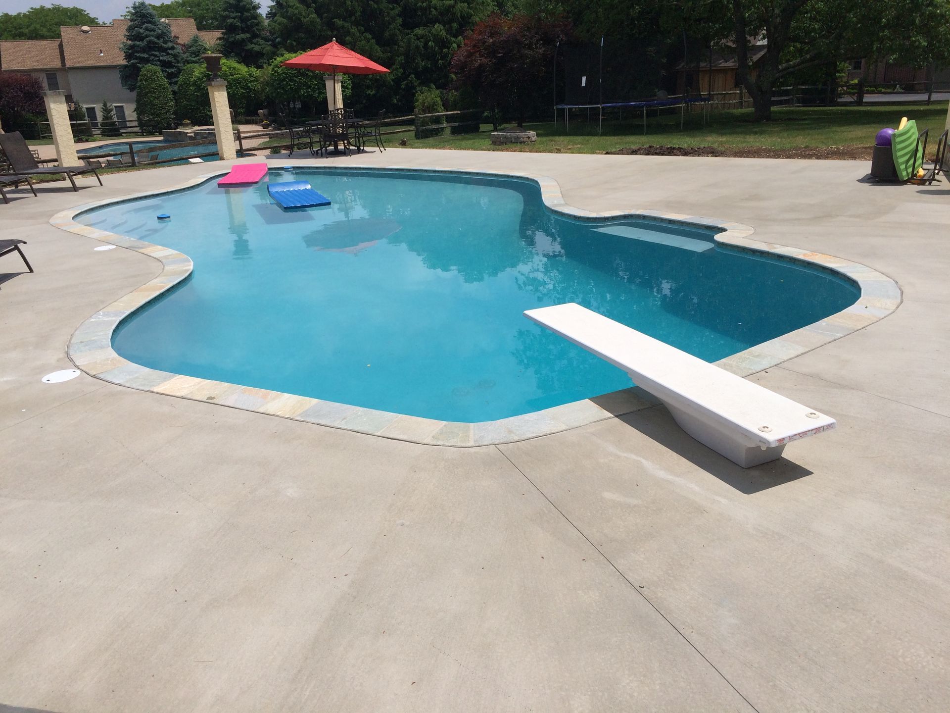 a large  stamped concrete swimming pool deck with a diving board in the middle