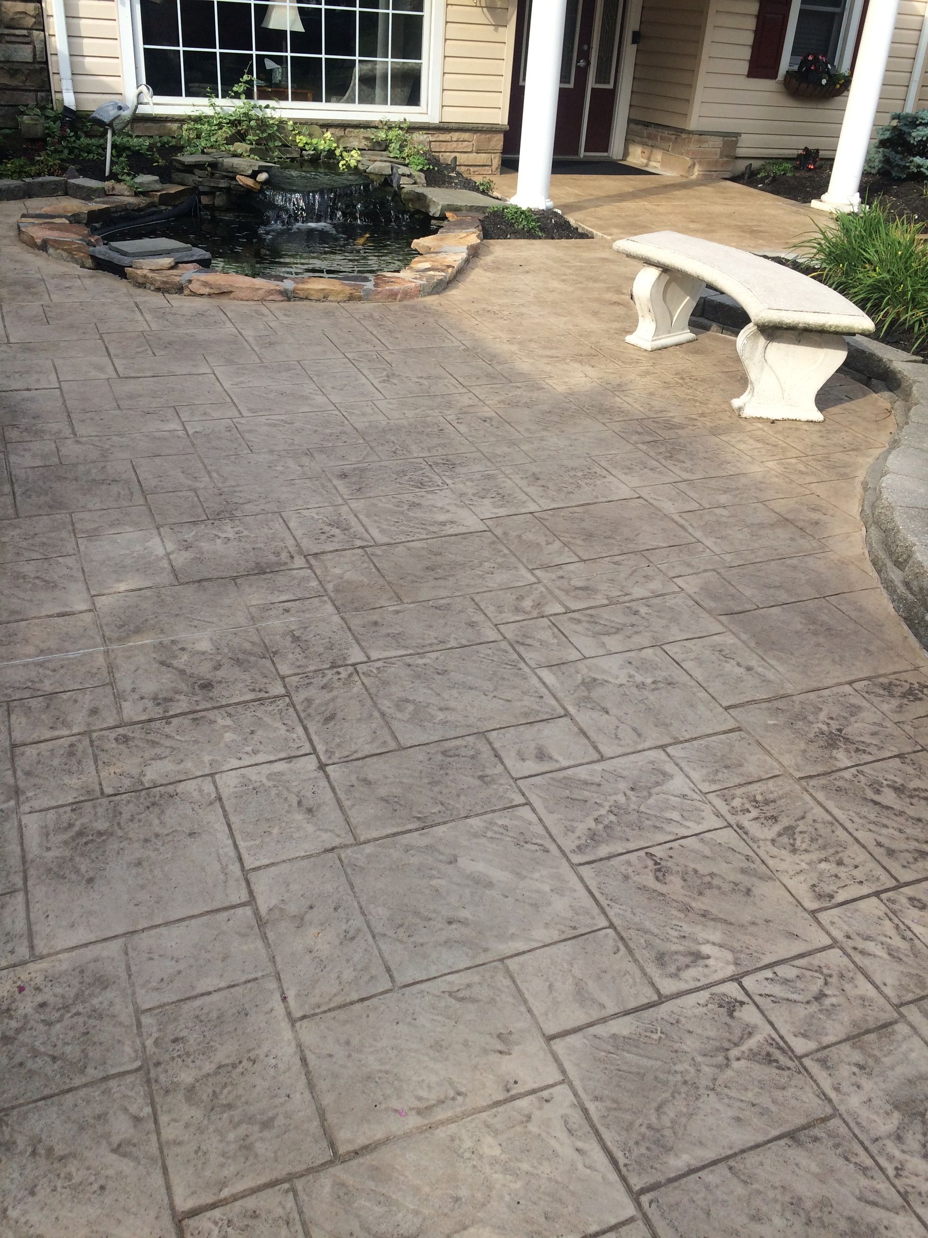 a  stamped concrete  patio that looks like slate with a bench and a pond in front of a house .