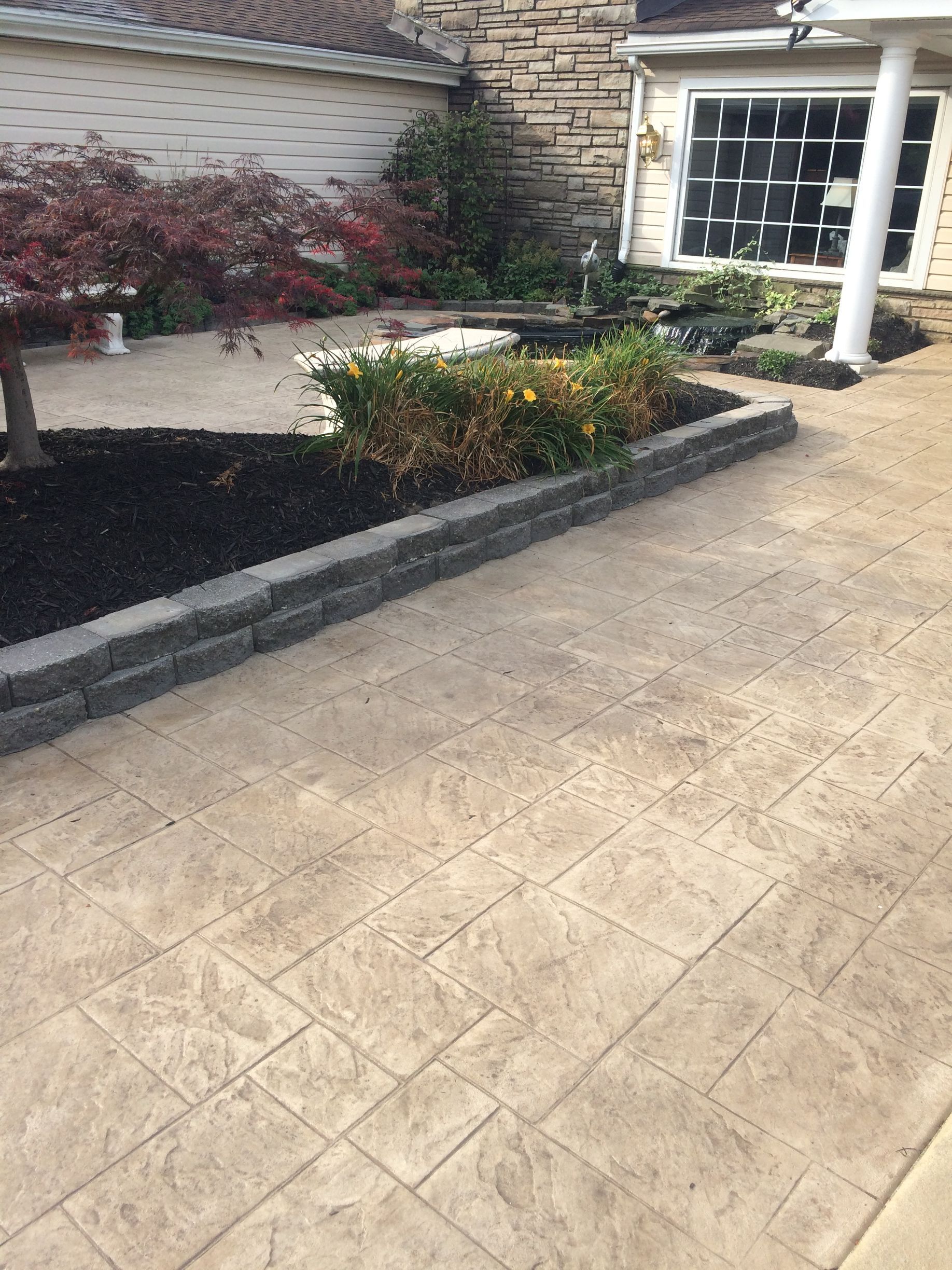 a stamped concrete walkway leading to a house with a brick wall in the background .