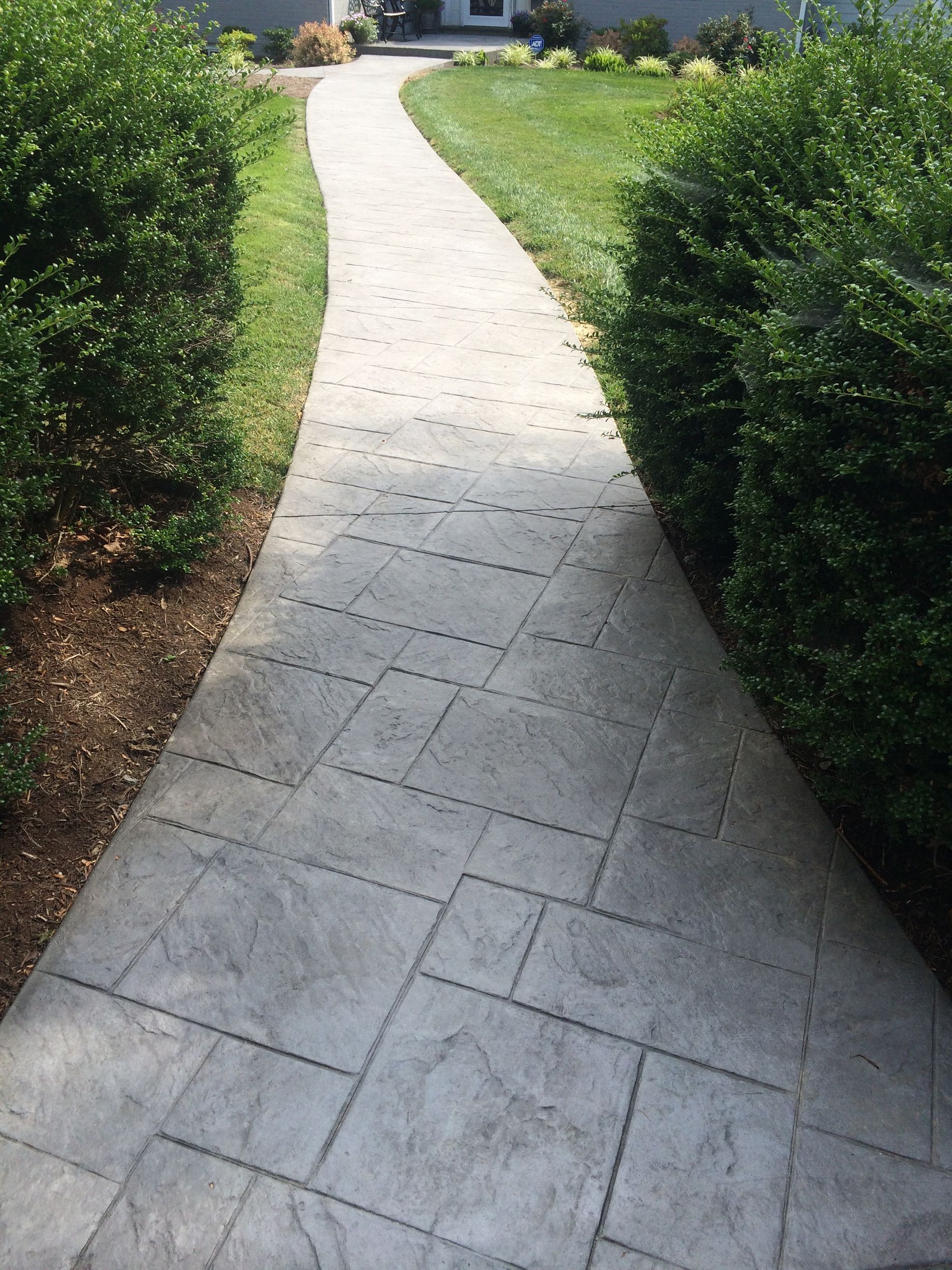 a  stamped concrete walkway leading to a house surrounded by bushes