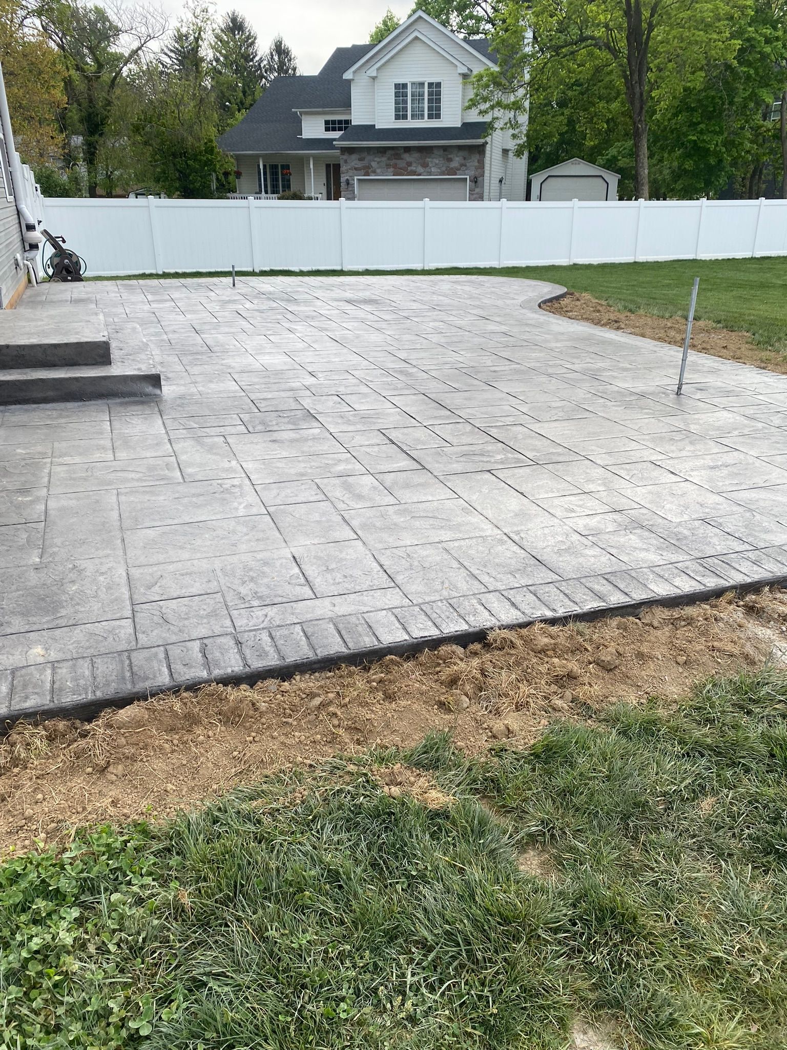 a  stamped concrete deck that looks like slate is being built in the backyard of a house with a white fence .