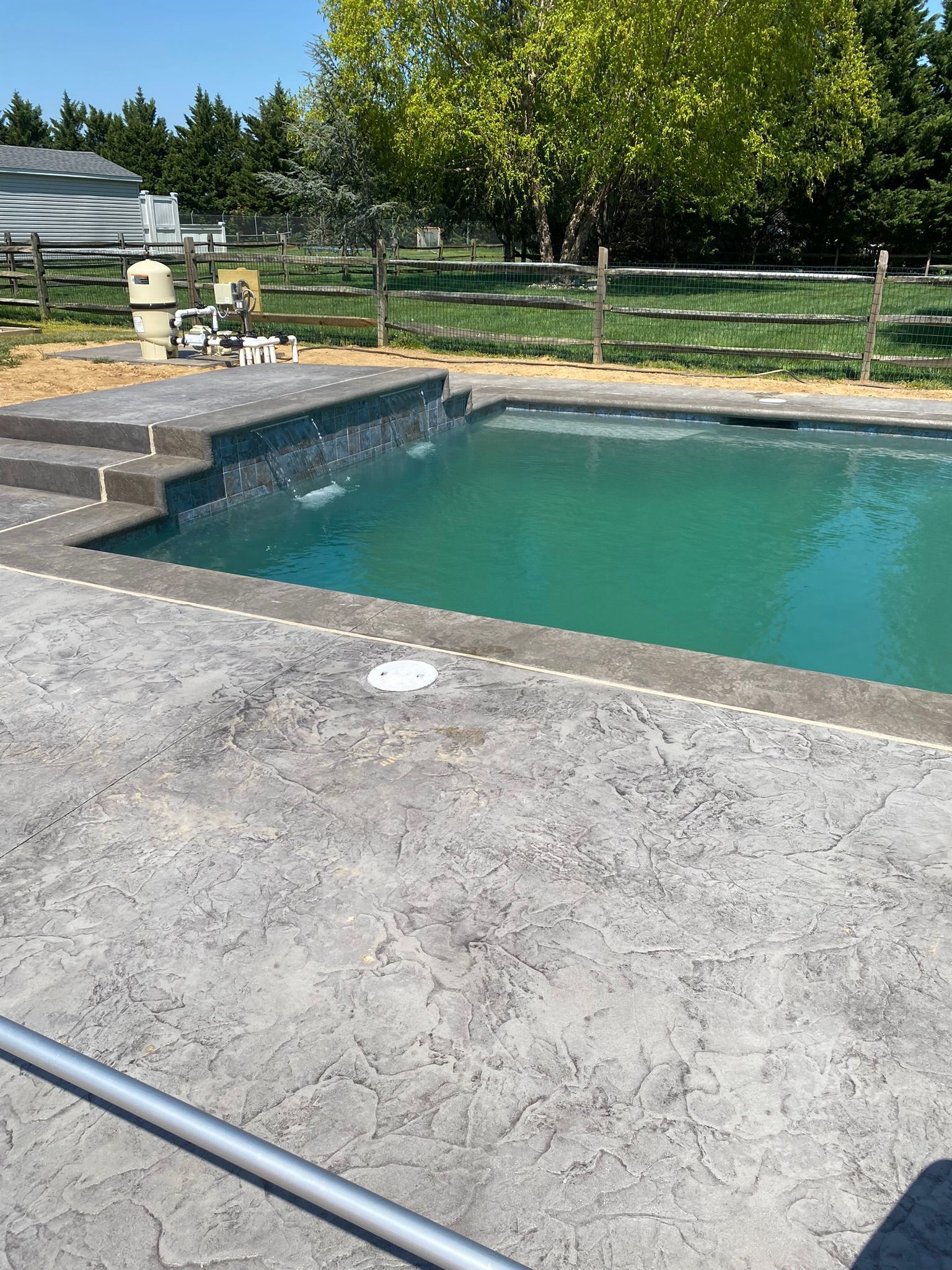 a large swimming pool is surrounded by a fence and a  stamped concrete  patio .