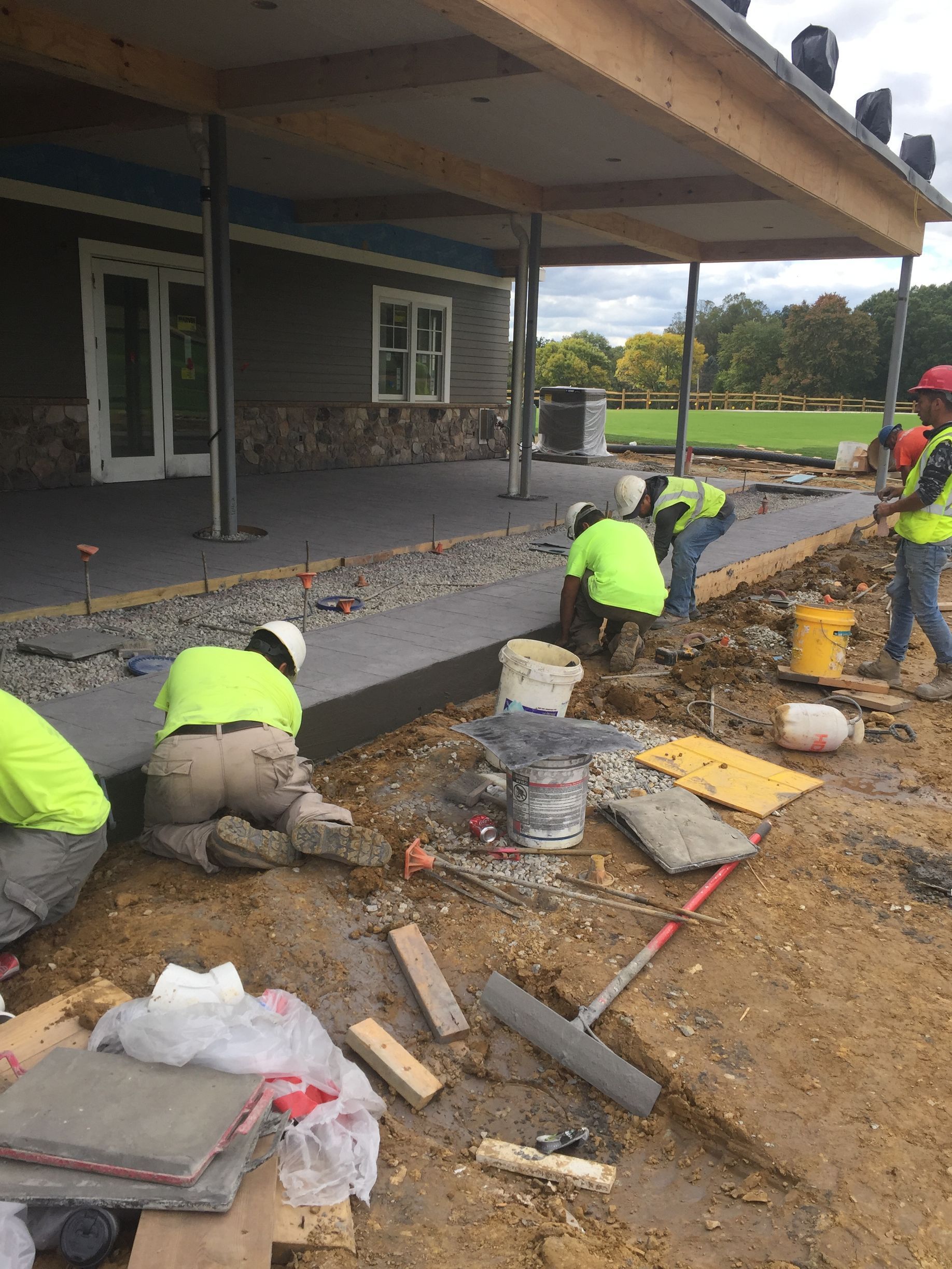 a group of construction workers are working on a concrete sidewalk in front of a building .