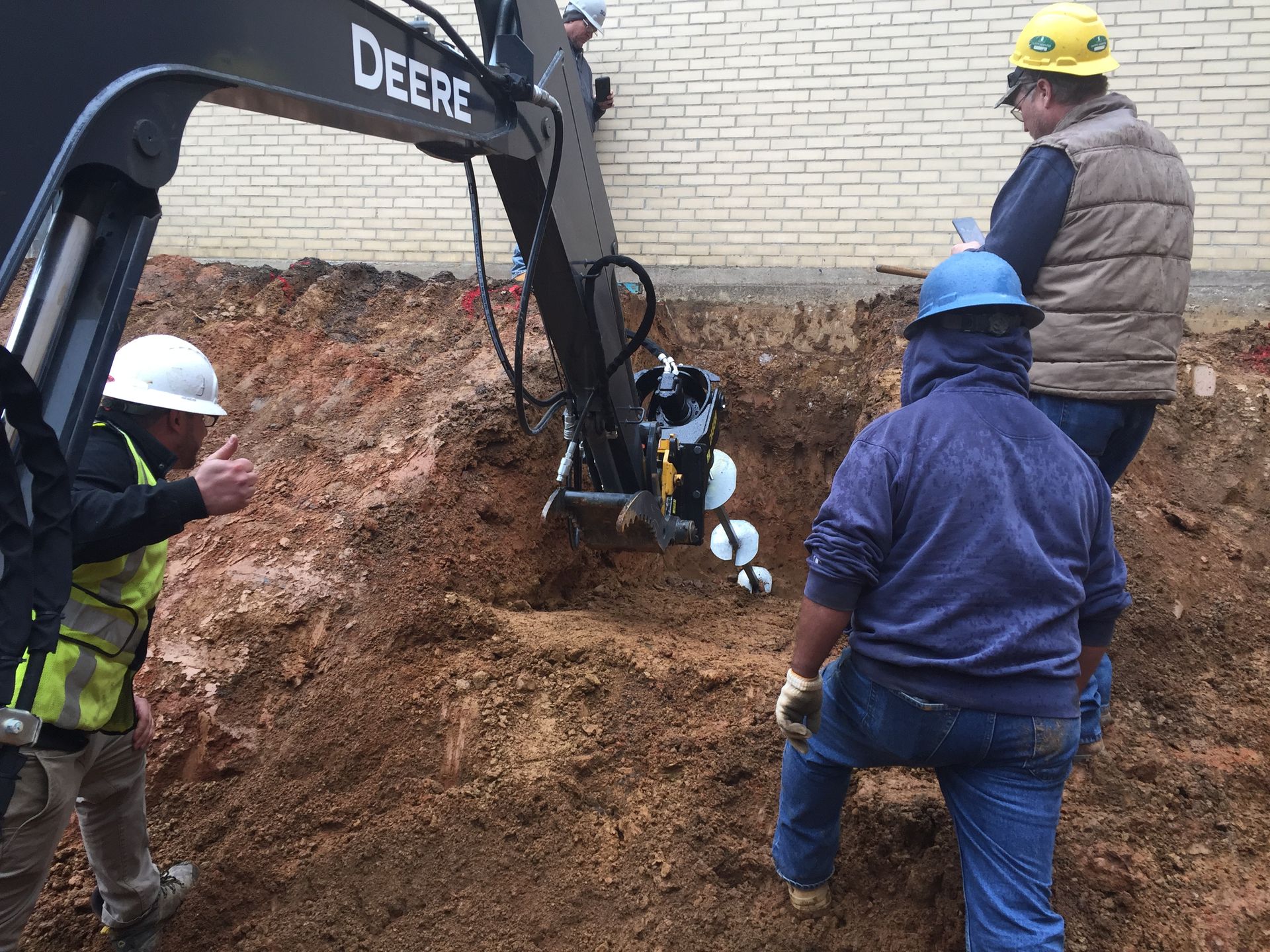 a group of construction workers are working on a deere excavator .