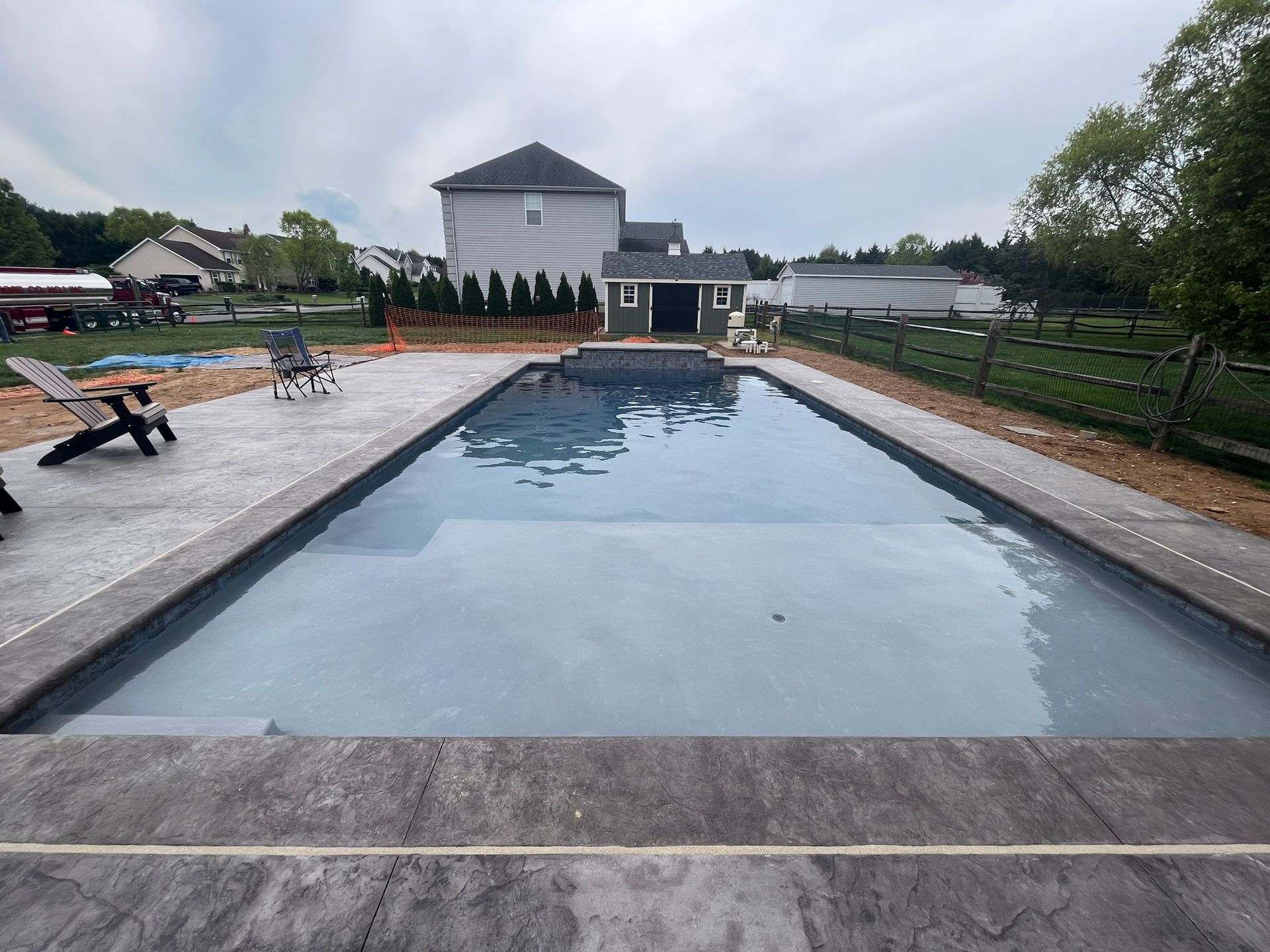 a large swimming pool with a  stamped concrete deck and house in the background
