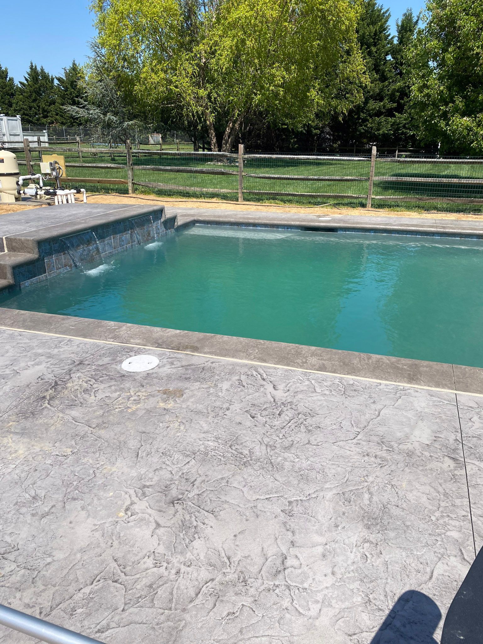 a large swimming pool with a  stamped concrete deck surrounded by trees and a fence .