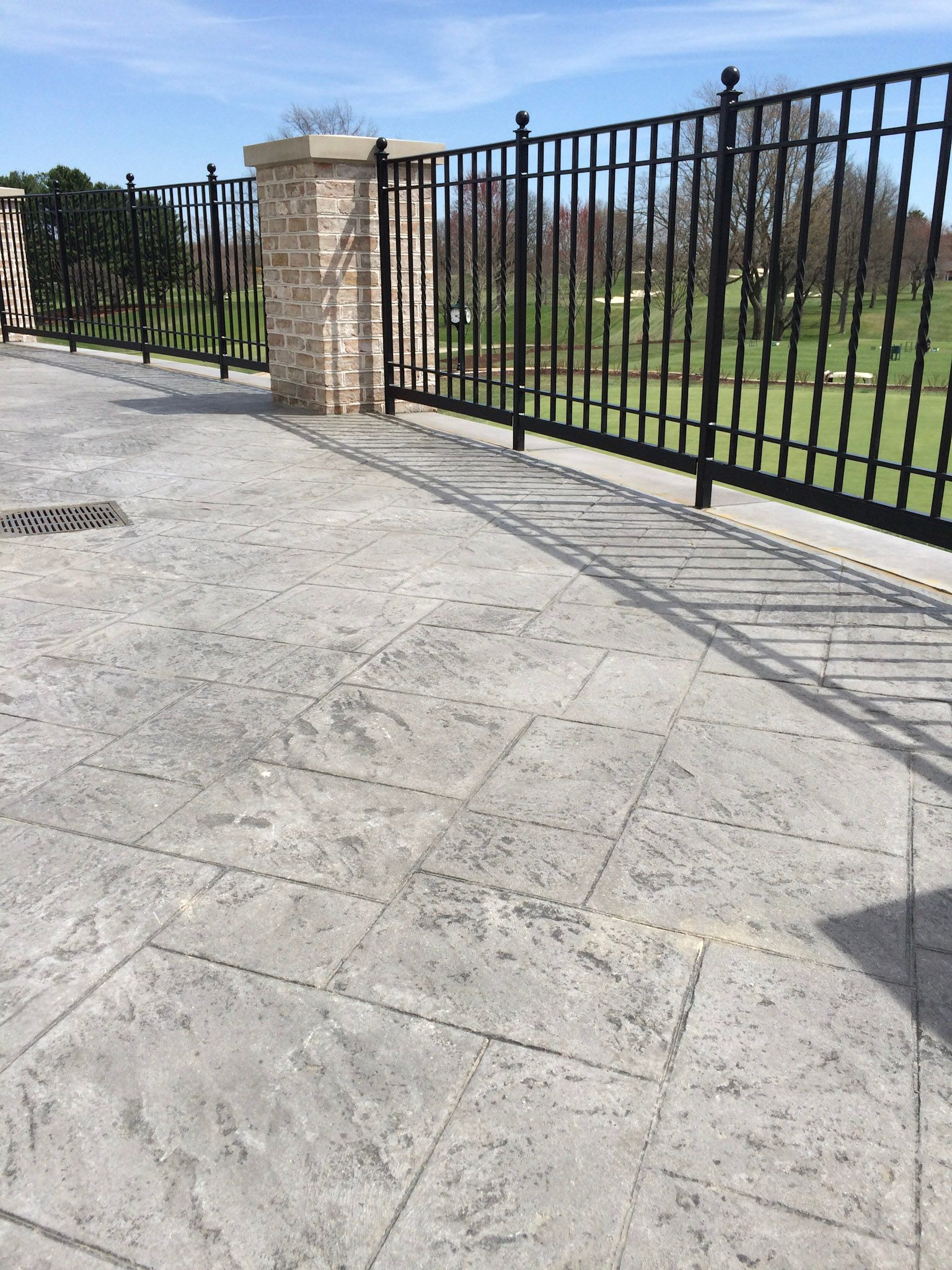 a  stamped concrete patio imitating slate pavers with a wrought iron fence surrounding it and a golf course in the background .