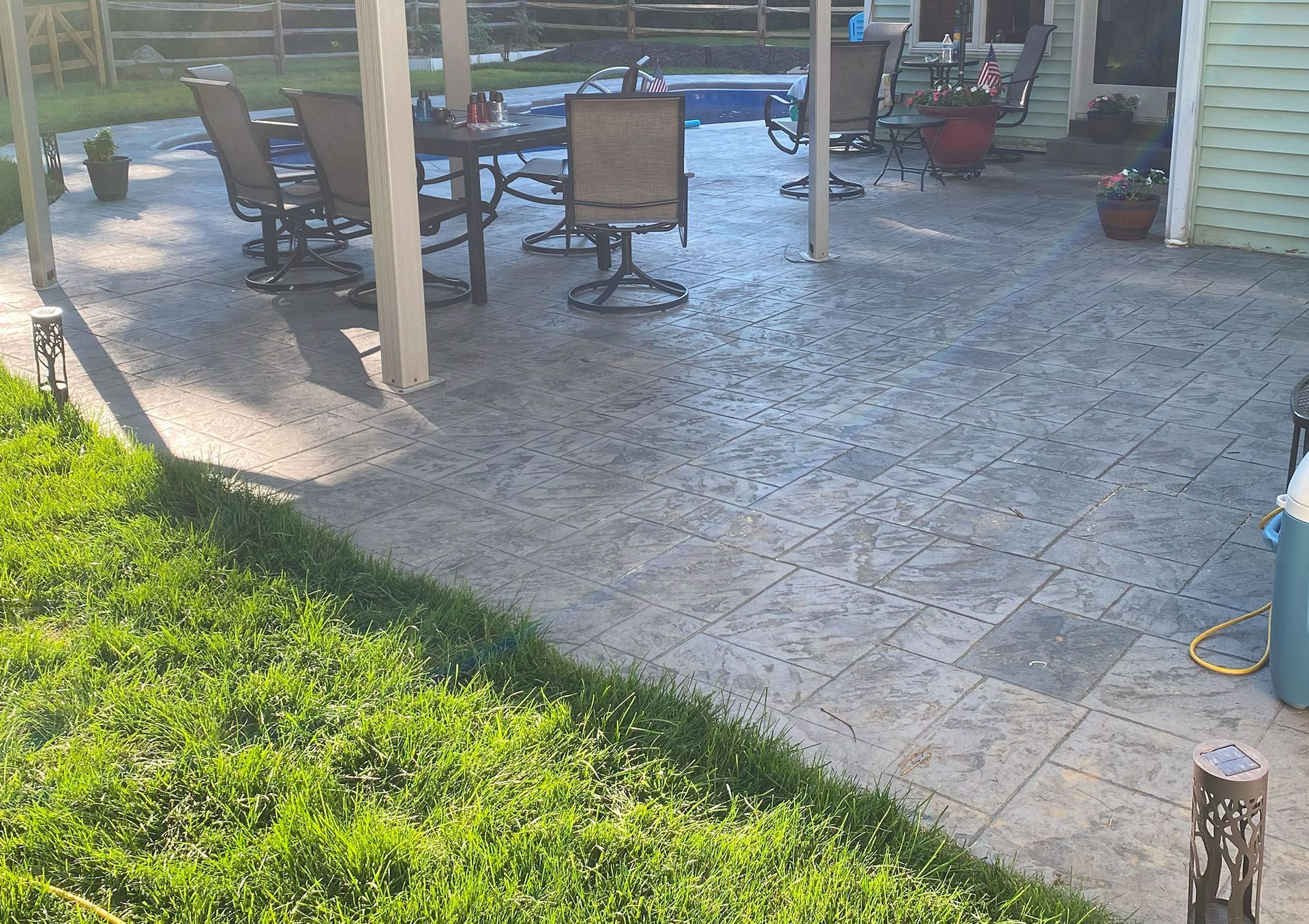 a  stamped concrete  patio with a table and chairs and a pool in the background