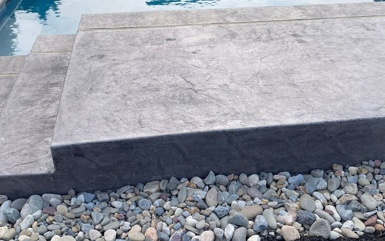 a  stamped concrete step next to a pool with rocks on the ground