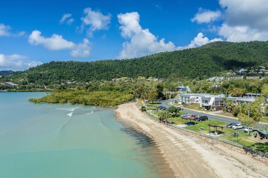 A Sandy Beach with Mountains in The Background and A Body of Water — Mi-ekka Designs in Cannonvale, QLD
