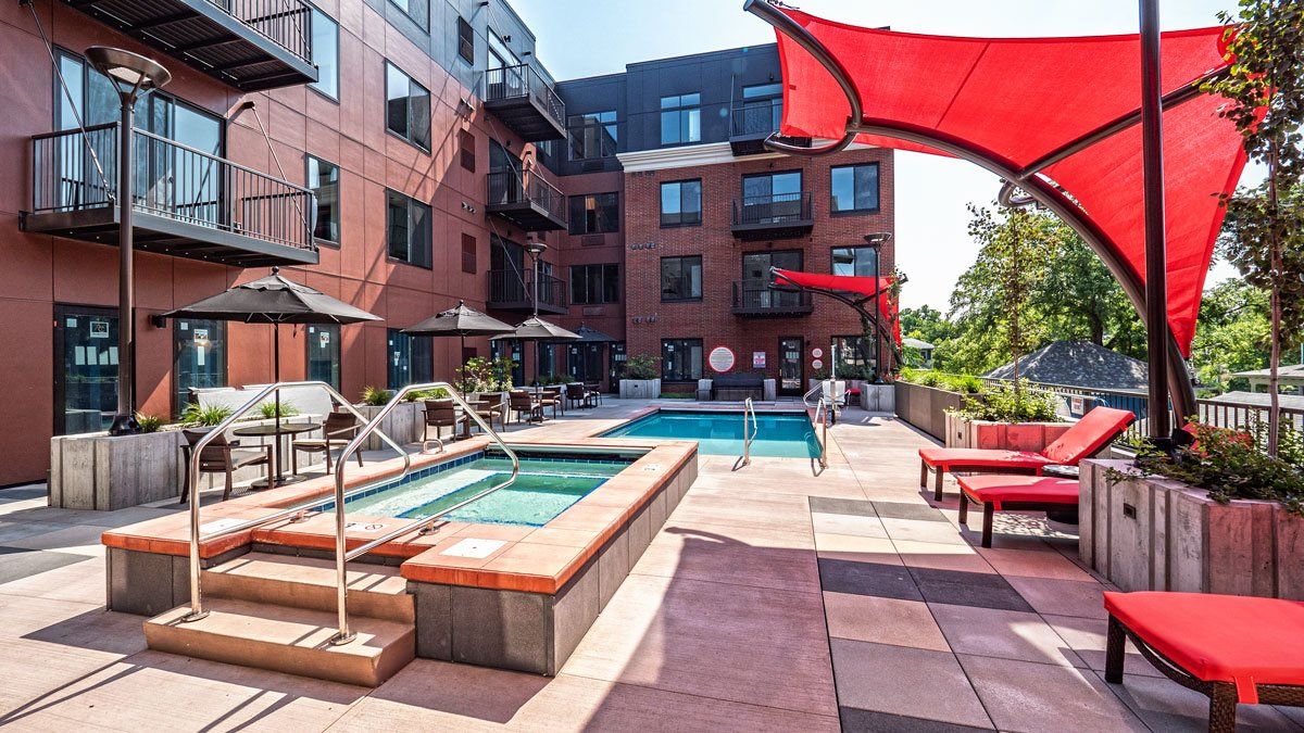 A large swimming pool surrounded by chairs and umbrellas in front of a brick building at Daymark Uptown Apartments.