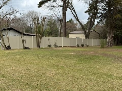 A tan vinyl privacy fence extends across a grassy backyard, with houses and trees visible in the background.