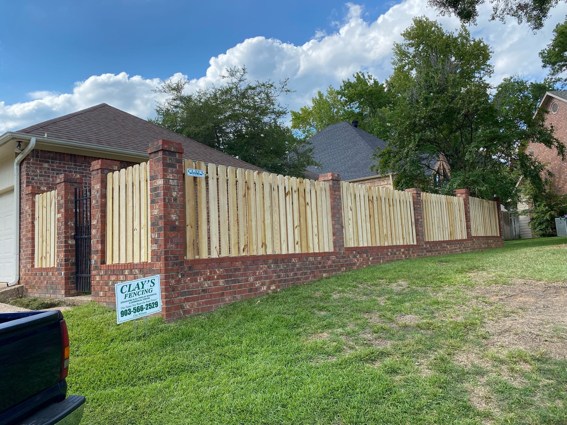 Brick and wood fence in front of a house on a grassy hill under a cloudy sky.