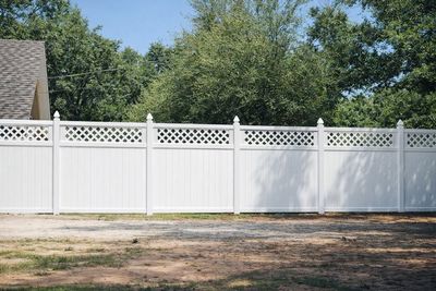 White vinyl fence in a grassy yard, with trees in the background.
