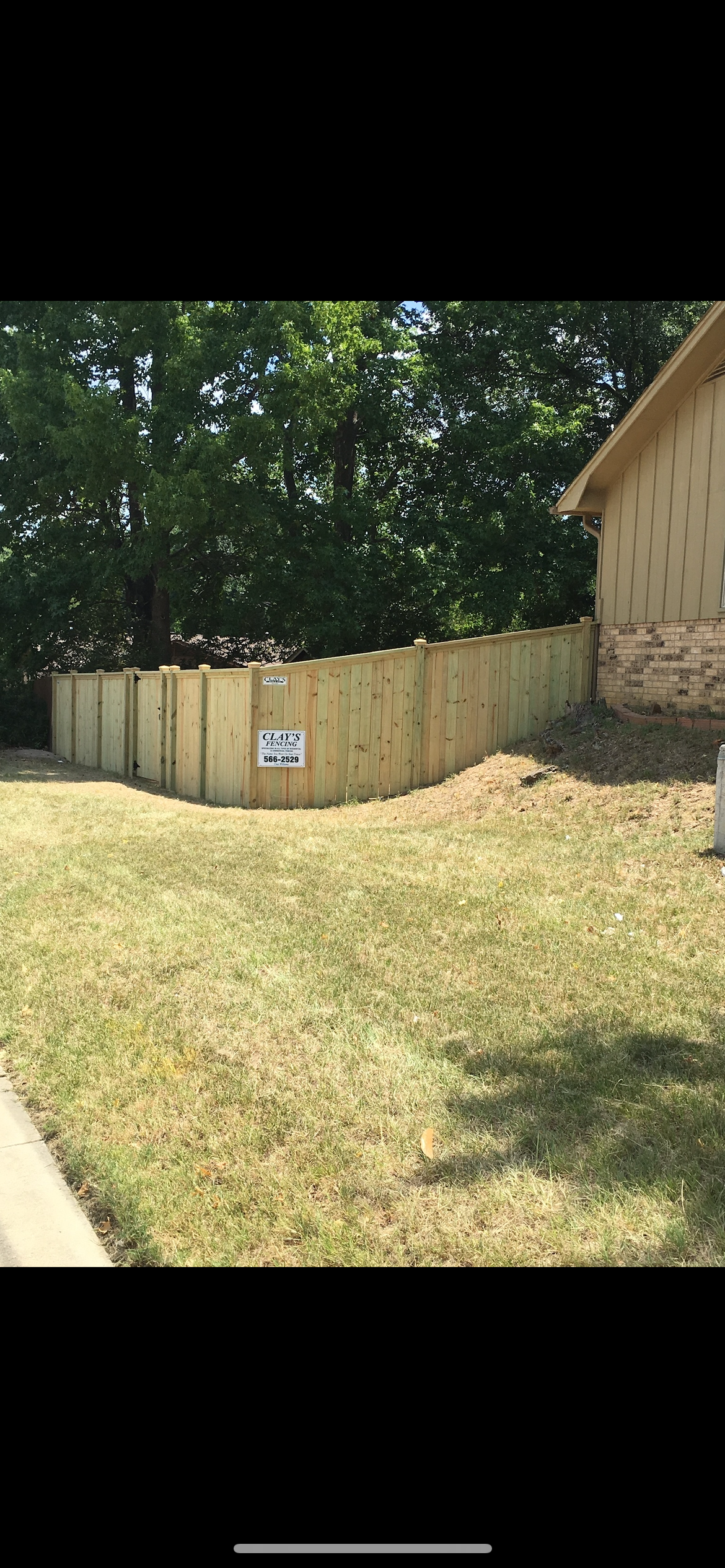 Wooden fence in a grassy yard next to a building and trees.