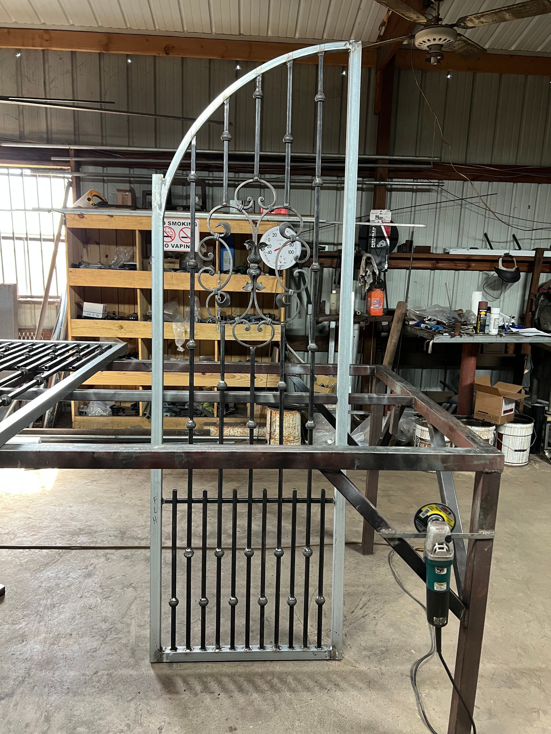 A metal gate in progress, with an arched top and vertical bars in a workshop setting.
