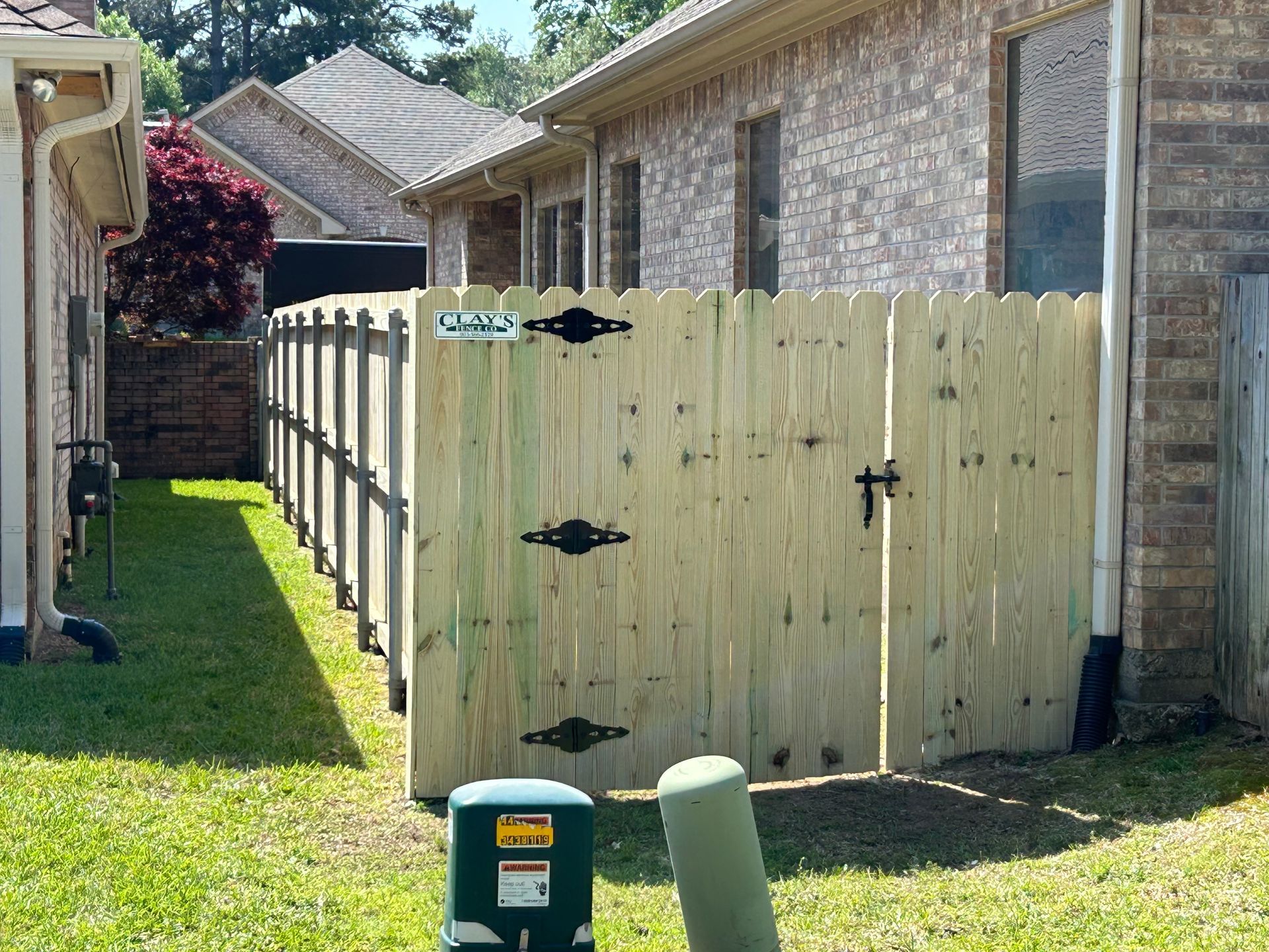 Wooden fence with gate between two brick buildings, on grassy lawn.