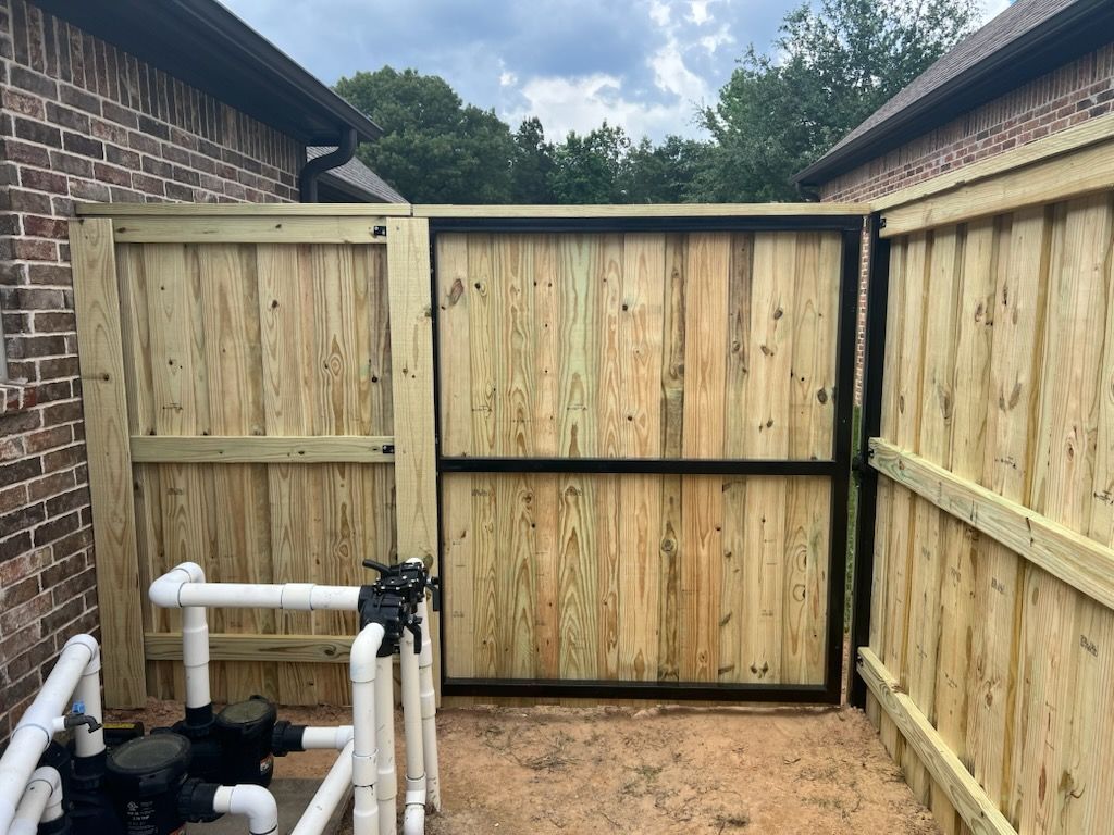 Wooden fence with black gate, near brick building, pool equipment visible.