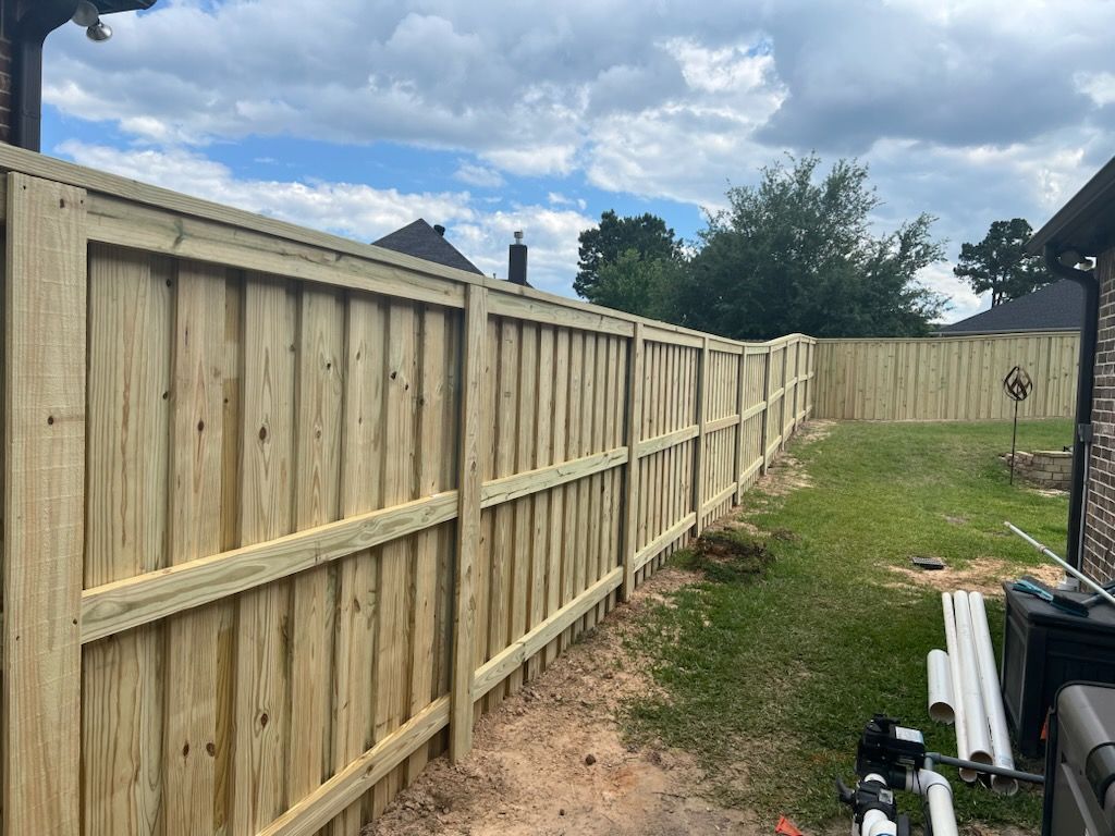 Wooden fence in a backyard, light brown, extending along a grassy area. Blue sky above.