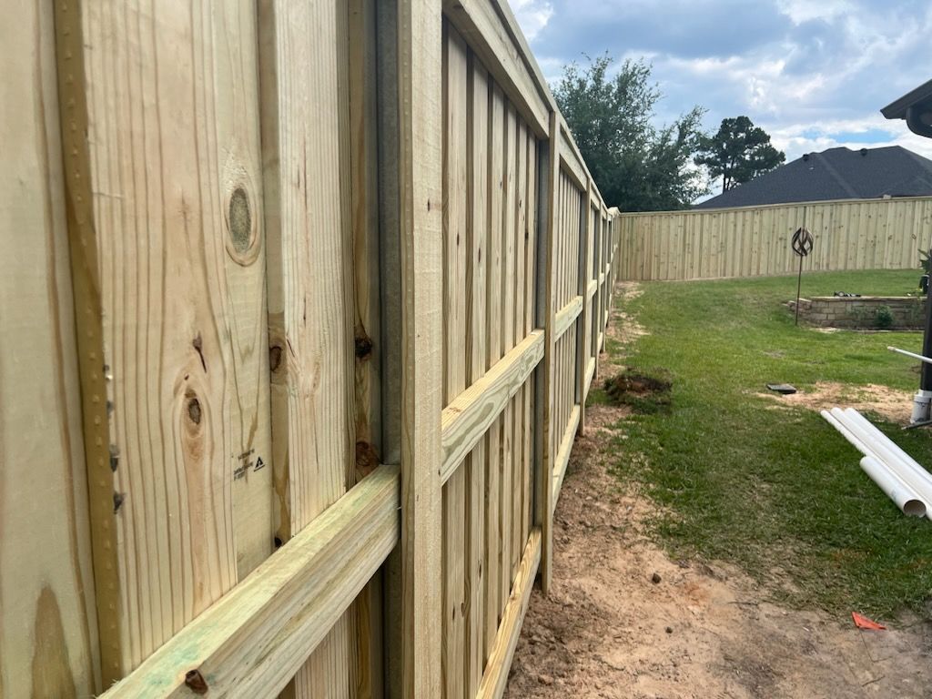 Wooden fence in a backyard, with green grass and a cloudy sky in the background.