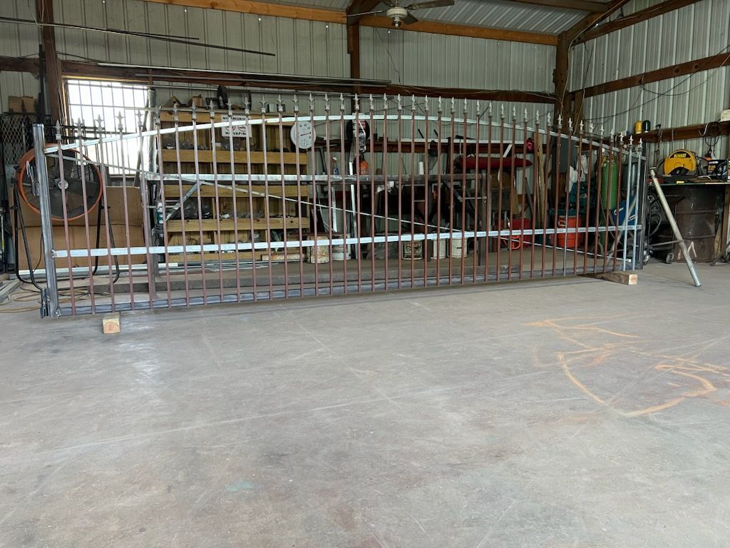 Metal gate under construction in a workshop with tools and welding equipment in the background.