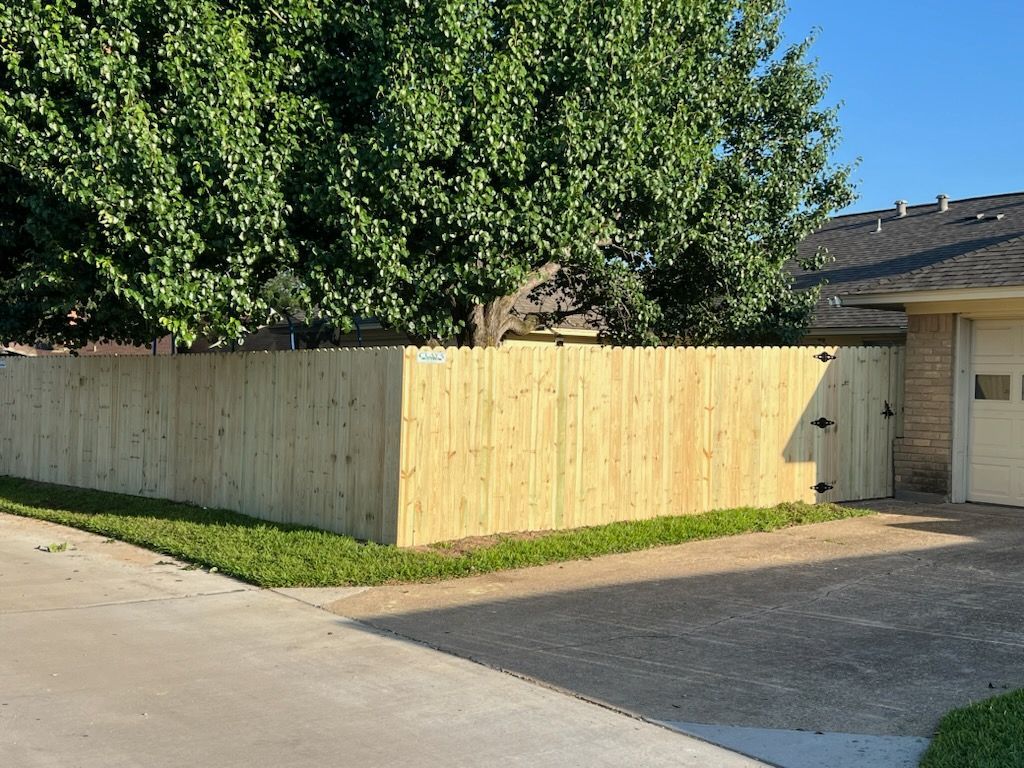 Wooden fence surrounds a yard, bordering a driveway and greenery.