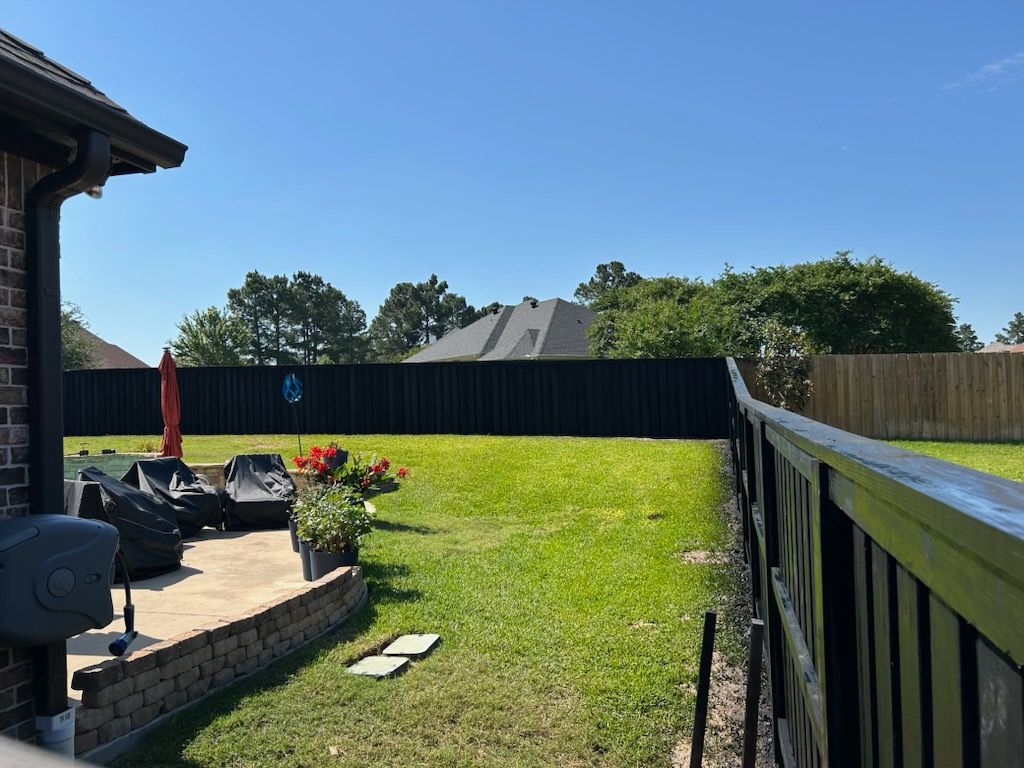 Backyard with black fence, patio, green grass, blue sky, and a red umbrella.