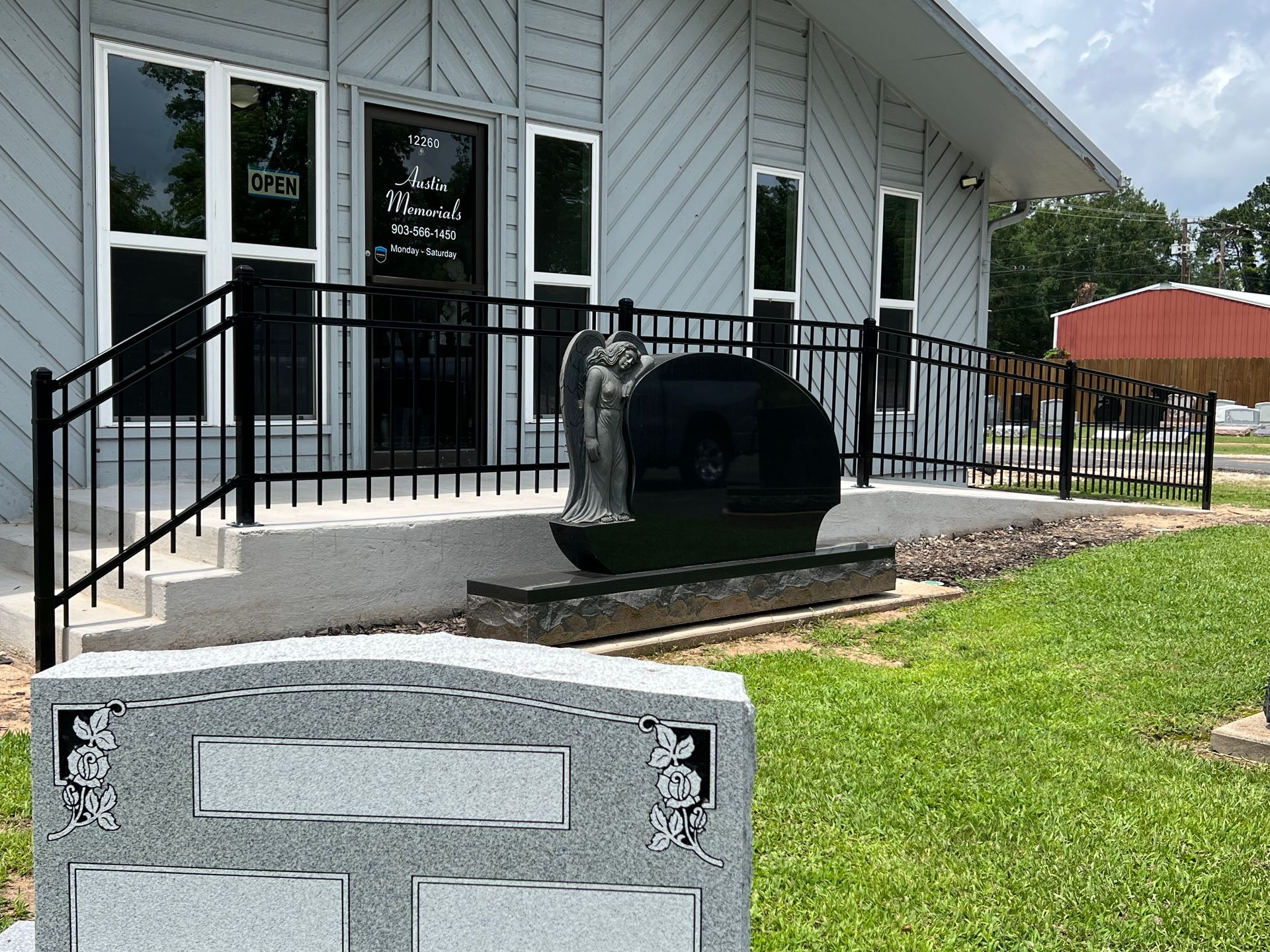 A funeral home with black railing, steps, and a large tombstone. Green grass in front.