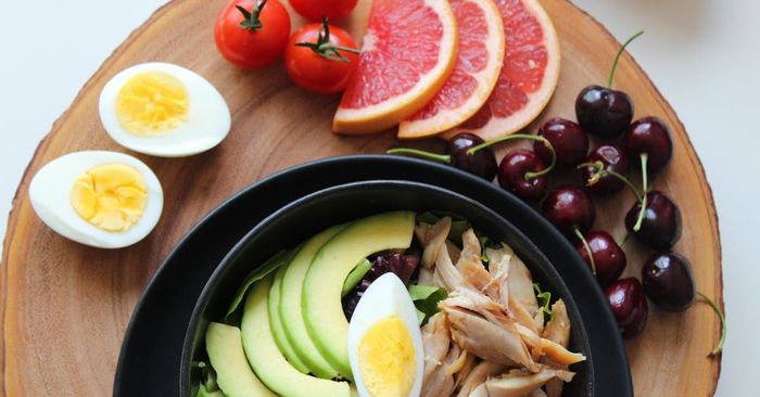 A bowl of food with eggs , grapefruit , tomatoes and cherries on a wooden cutting board.