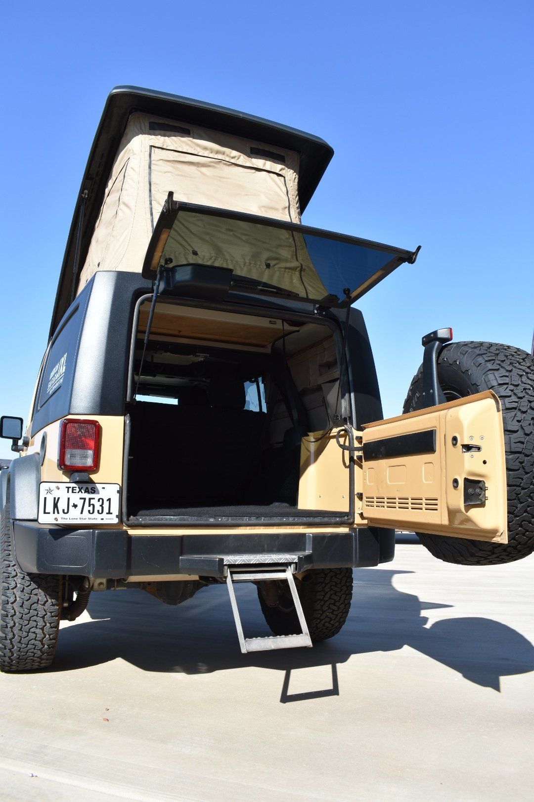 The back of a jeep with the door open and a step attached to it.