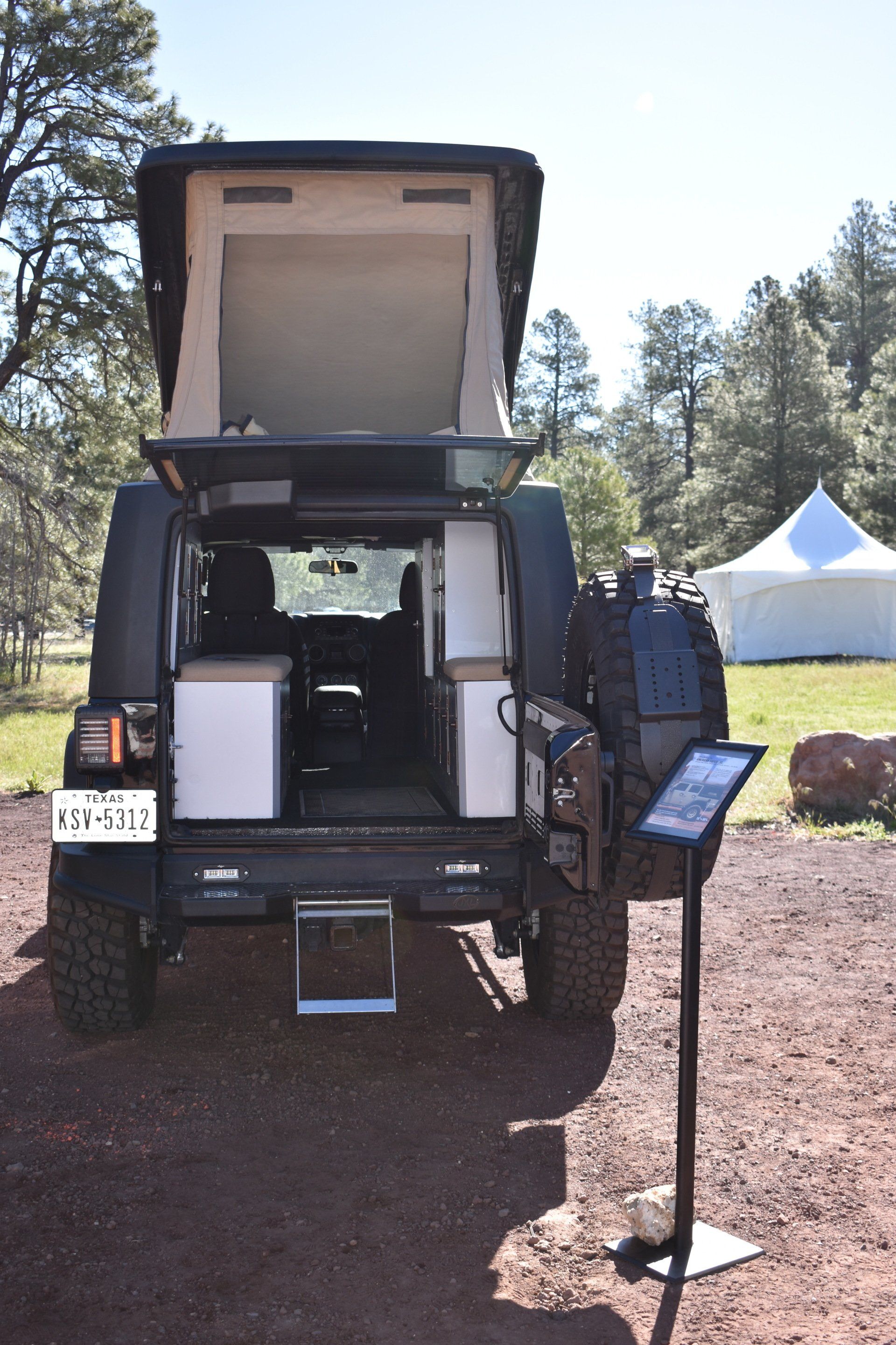 A JXL with a tent popped up is parked in a dirt field.