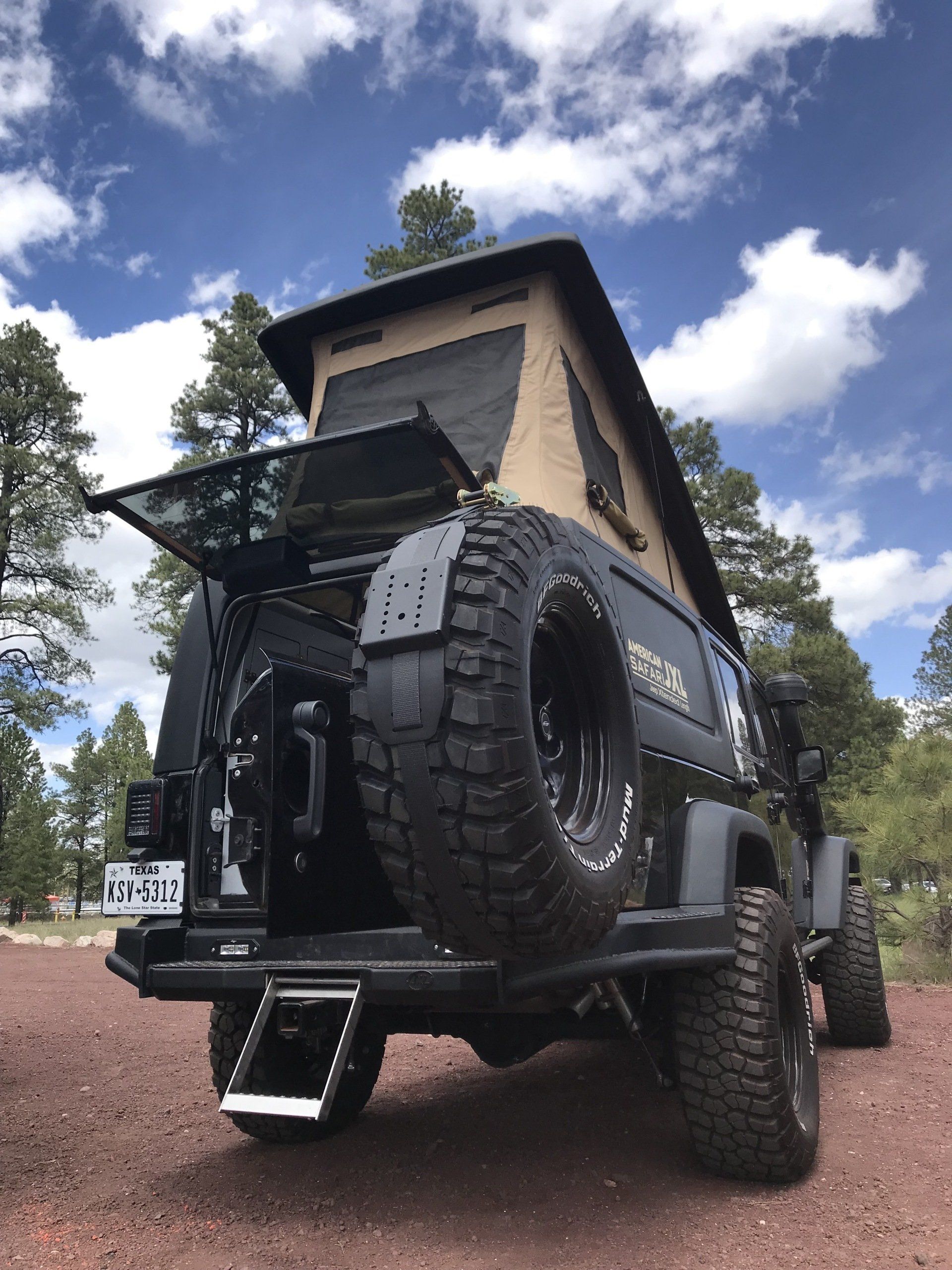 A JXL with a tent on top of it is parked on a dirt road.