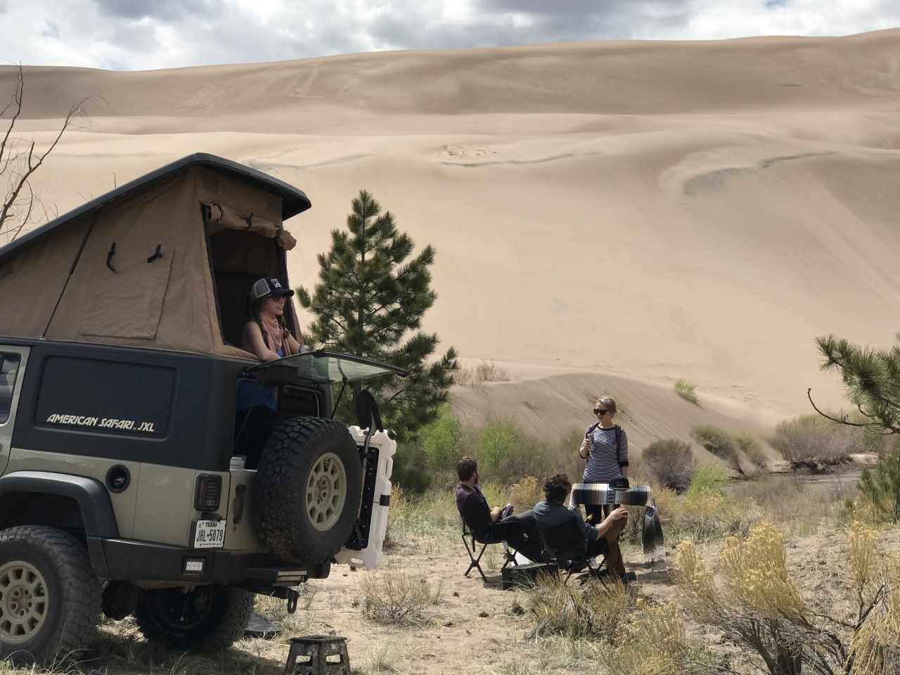 A group of people are sitting in front of a JXL with a tent on top of it.
