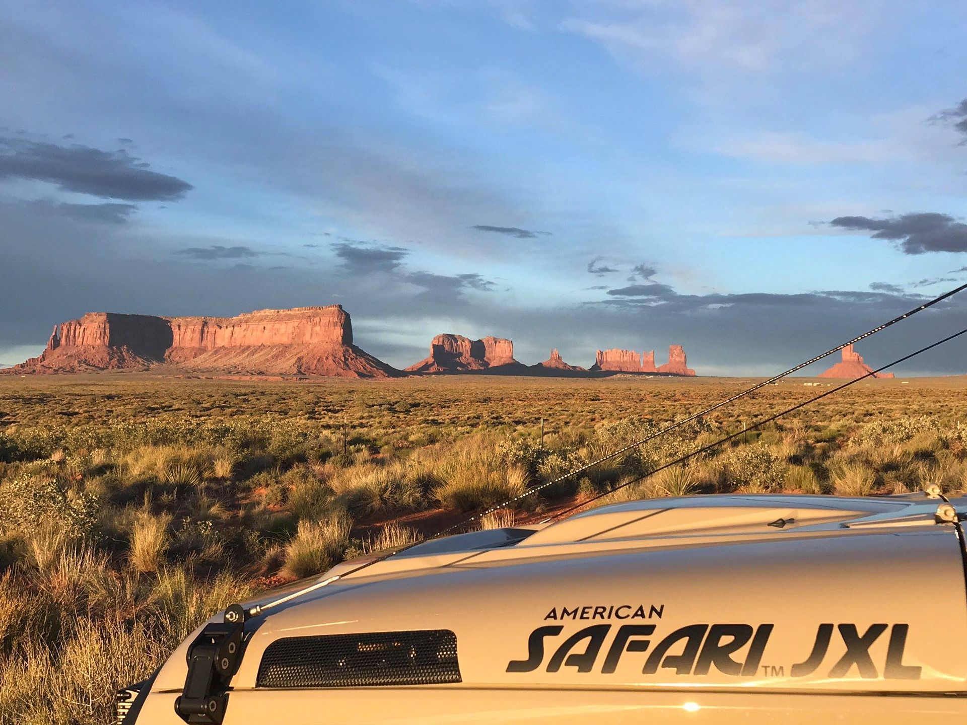 A safari jeep is parked in the desert with mountains in the background.