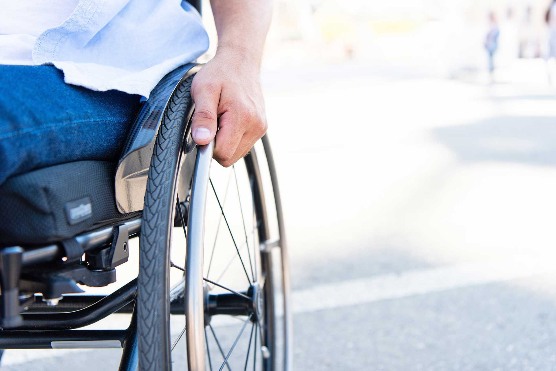 Nahaufnahme eines Rollstuhlfahers auf einer Straße mit der Hand am Reifen