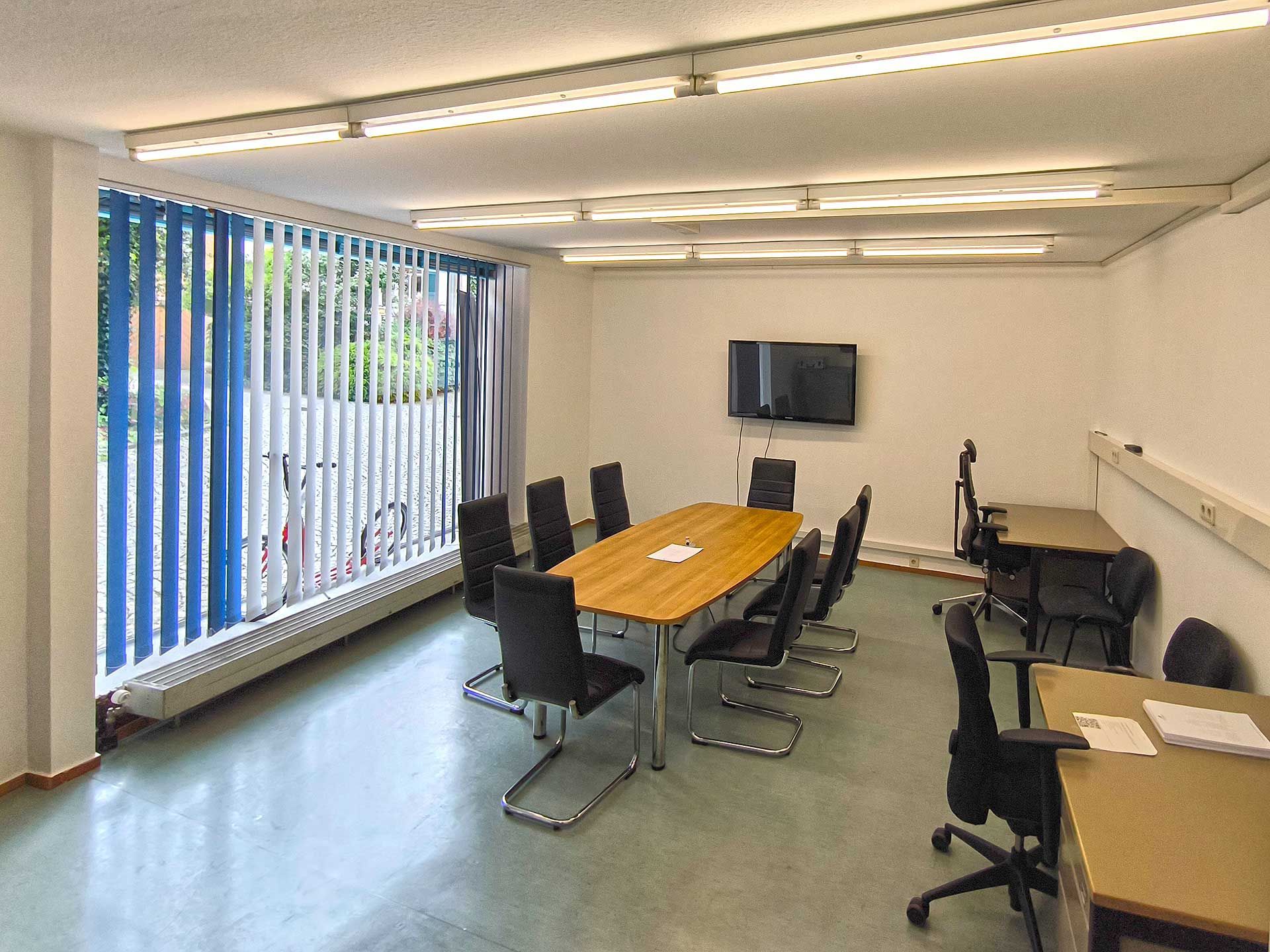 Der kleine Konferenzraum mit einem großen Tisch und 8 Stühlen sowie zwei Schreibtischen an der Wand