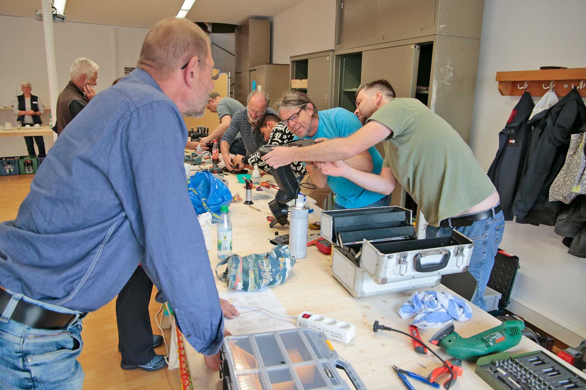 Eine Gruppe Personen beugt sich über ein elektrisches Gerät um es zu reparieren